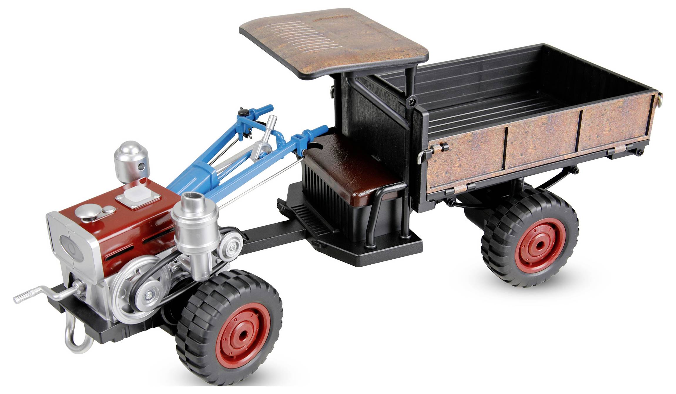 Speelgoed traptractor met een motor aan de voorkant en een blauwe sleephaak die een kleine zwart- en roestkleurige aanhanger met een kap trekt.