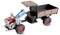 Speelgoed traptractor met een motor aan de voorkant en een blauwe sleephaak die een kleine zwart- en roestkleurige aanhanger met een kap trekt.