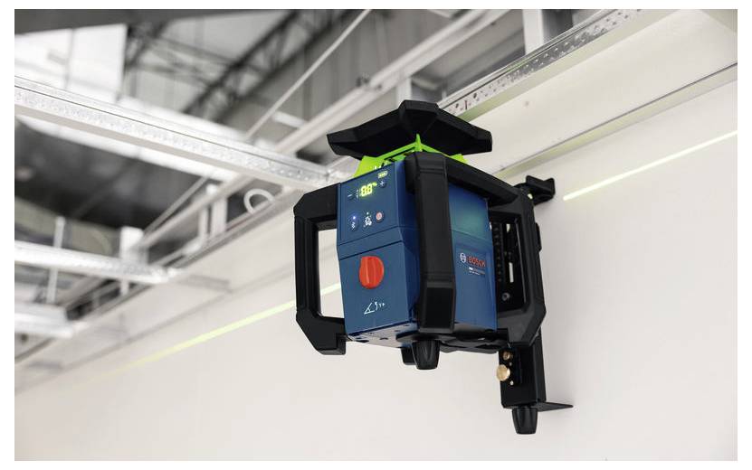 Laserniveau op een wandbeugel gemonteerd dat groene uitlijningslijnen in een industrieel interieur projecteert.
