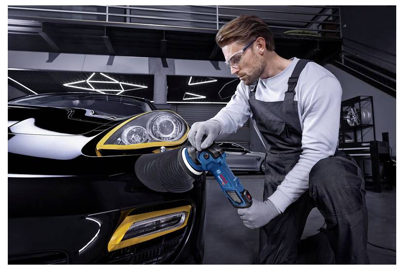 Monteur die de voorkoplamp van een zwarte sportauto in een garage met een handbuffer polijst.