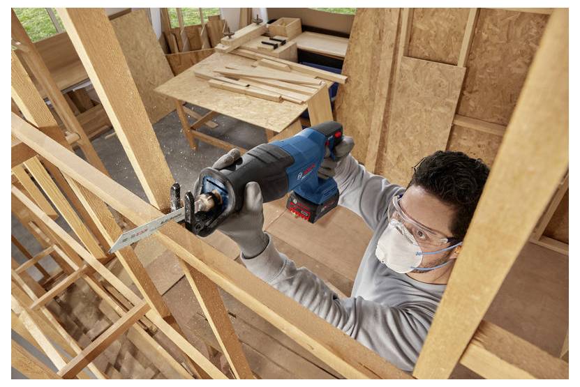 Bouwvakker met masker en veiligheidsbril gebruikt een reciprocerende zaag om houten constructiewerk te zagen in een huis in aanbouw.