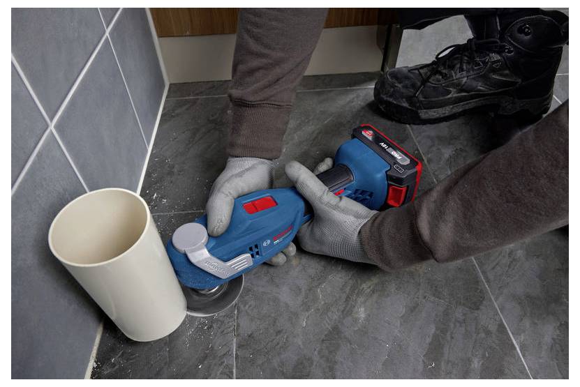 Persoon die een blauw handheld elektrisch gereedschap gebruikt om naast een muur en een beker in een betegelde kamer de vloer te slijpen of te polijsten.