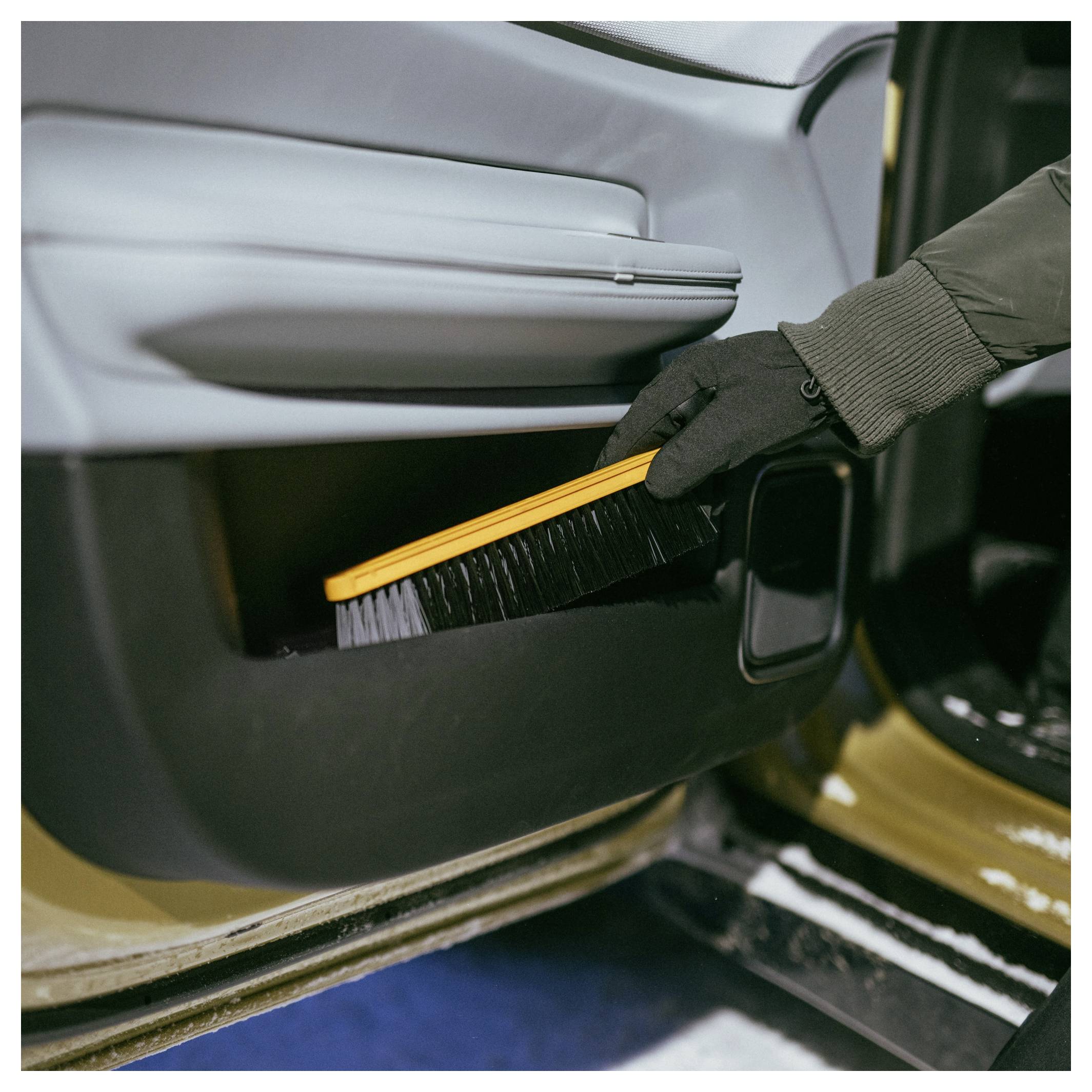 Behandschoenende hand gebruikt een borstel om stof van het onderste interieurpaneel van een autodeur schoon te maken.