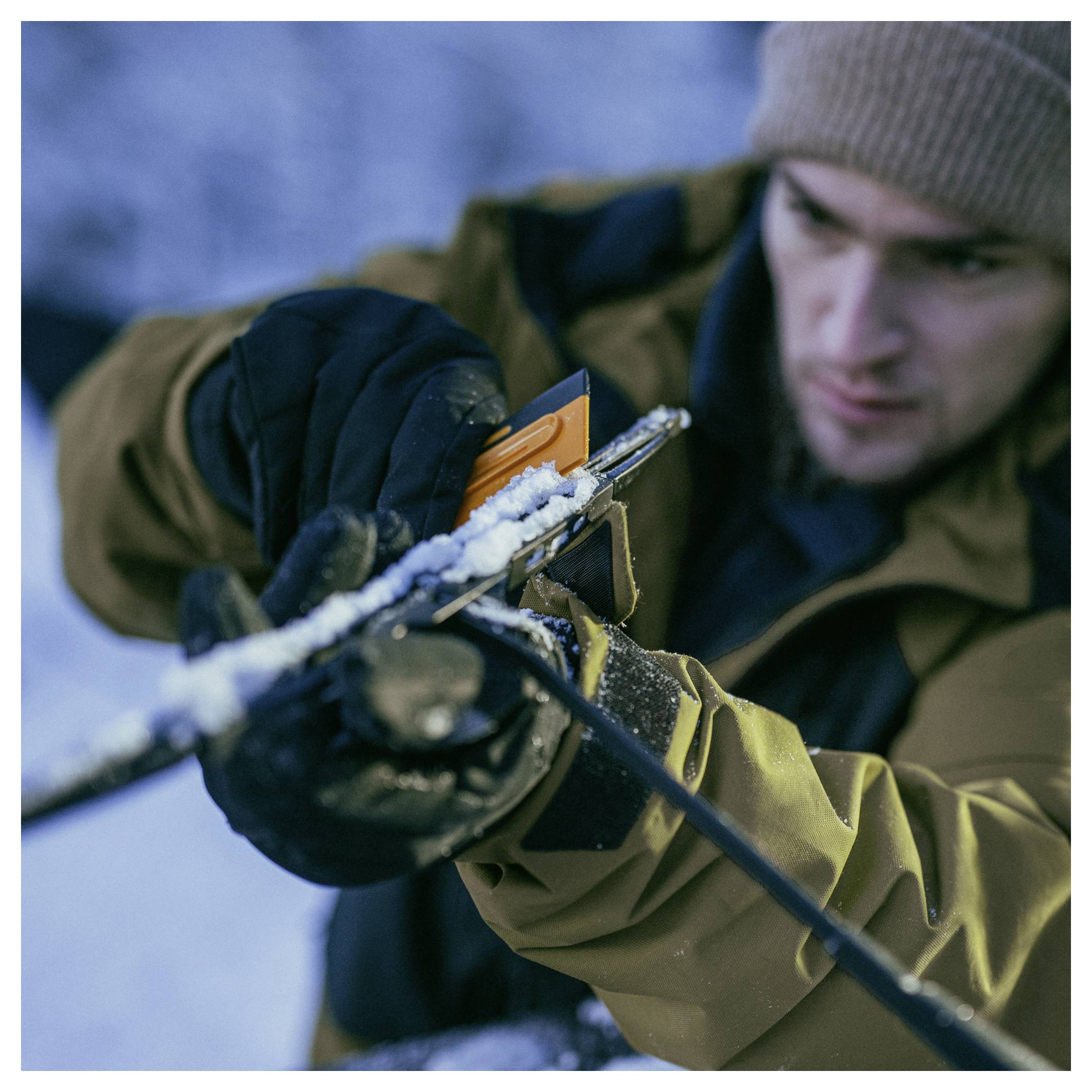 Close-up van een man in winterkleding die sneeuw van een geweer schoonmaakt buiten.