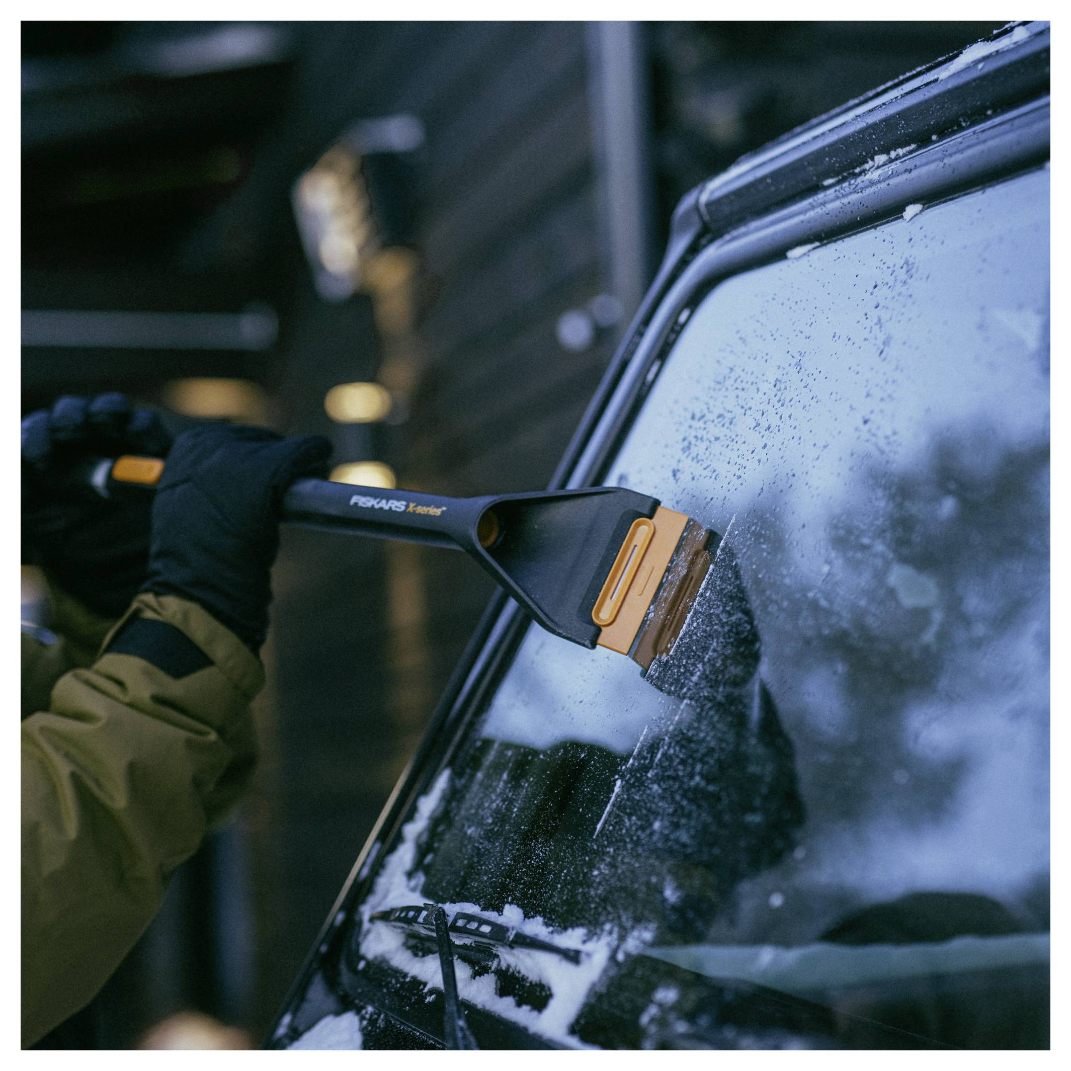 Persoon met handschoenen schabt ijs en sneeuw van een autoruitenwisser met een borstschraper.