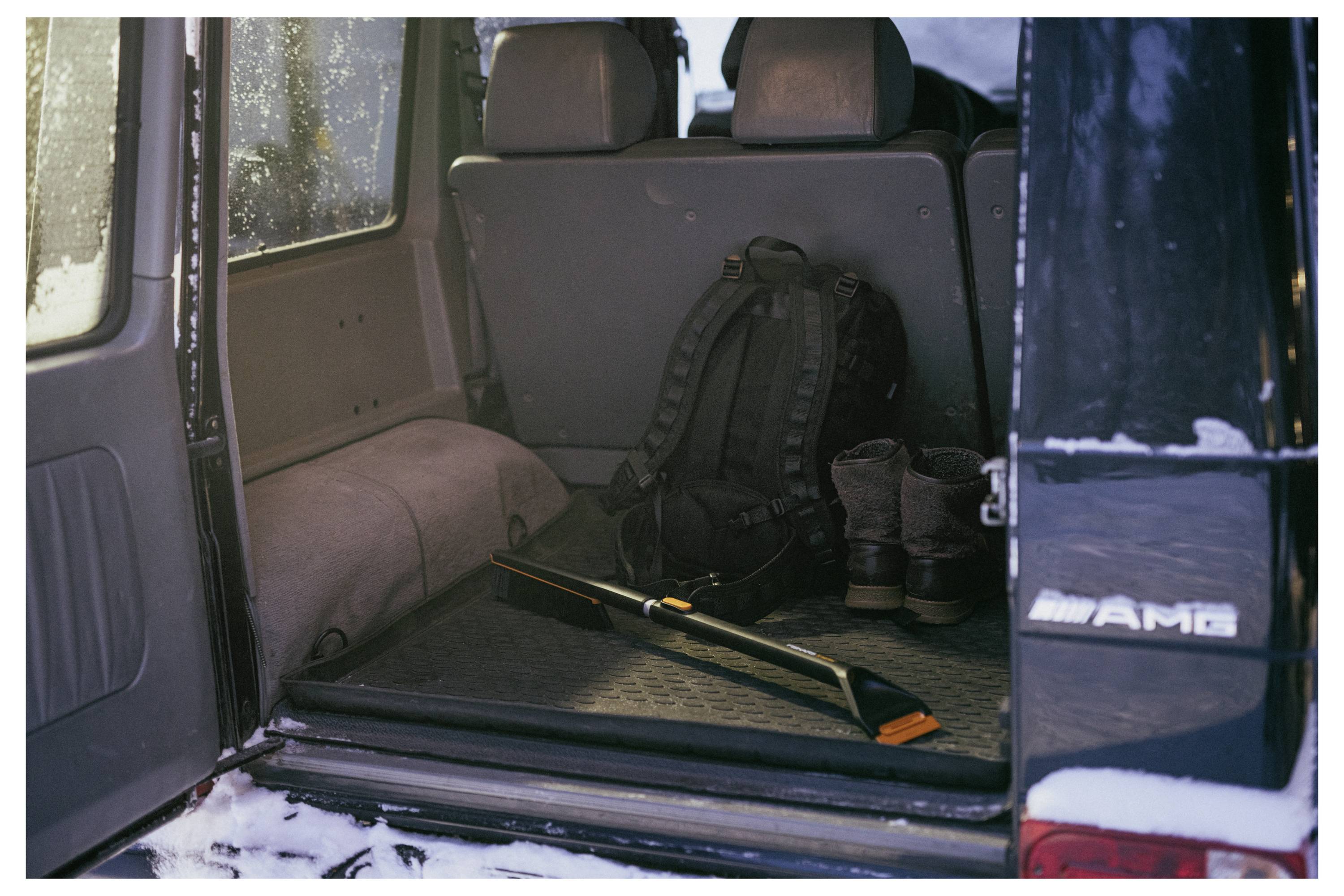 Open SUV-kofferbak met een rugzak, laarzen en een gereedschap of trekking-stok op de laadvloer.