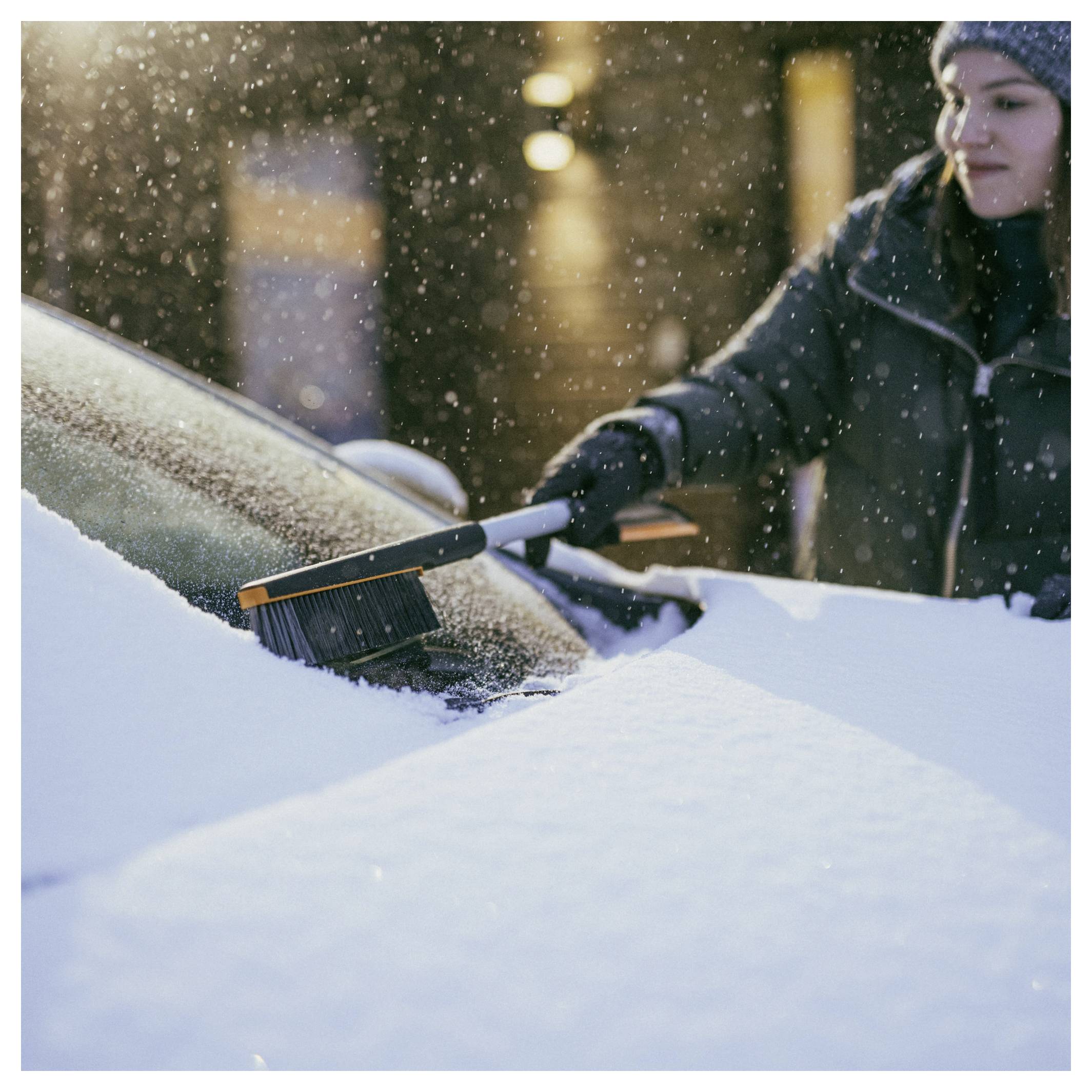 Persoon die sneeuw van een autoruit verwijdert met een borstel tijdens sneeuwval buiten.