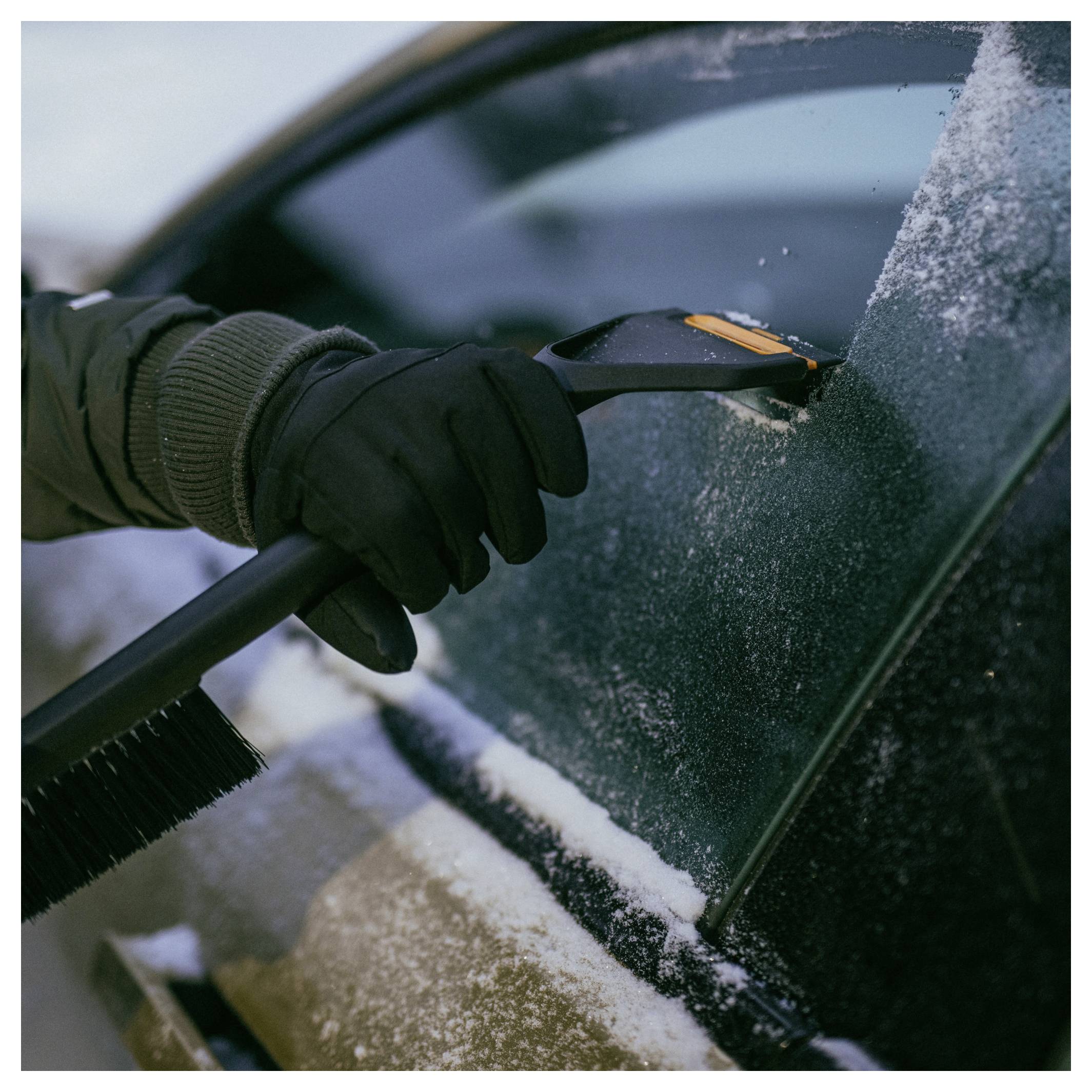 Gehandschoende hand die een ijskrabber gebruikt om rijp en sneeuw van een autoruit te verwijderen.