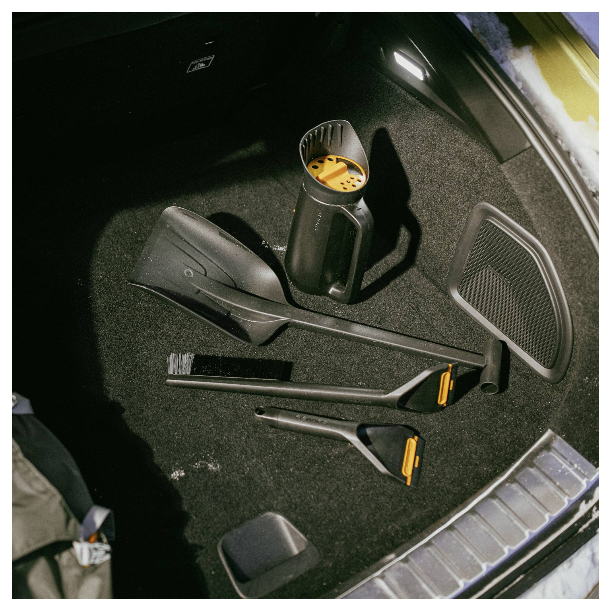 Autodak met uitgepackte stofzuigeronderdelen op het tapijt, inclusief slangen, borstels en een stofcontainer.