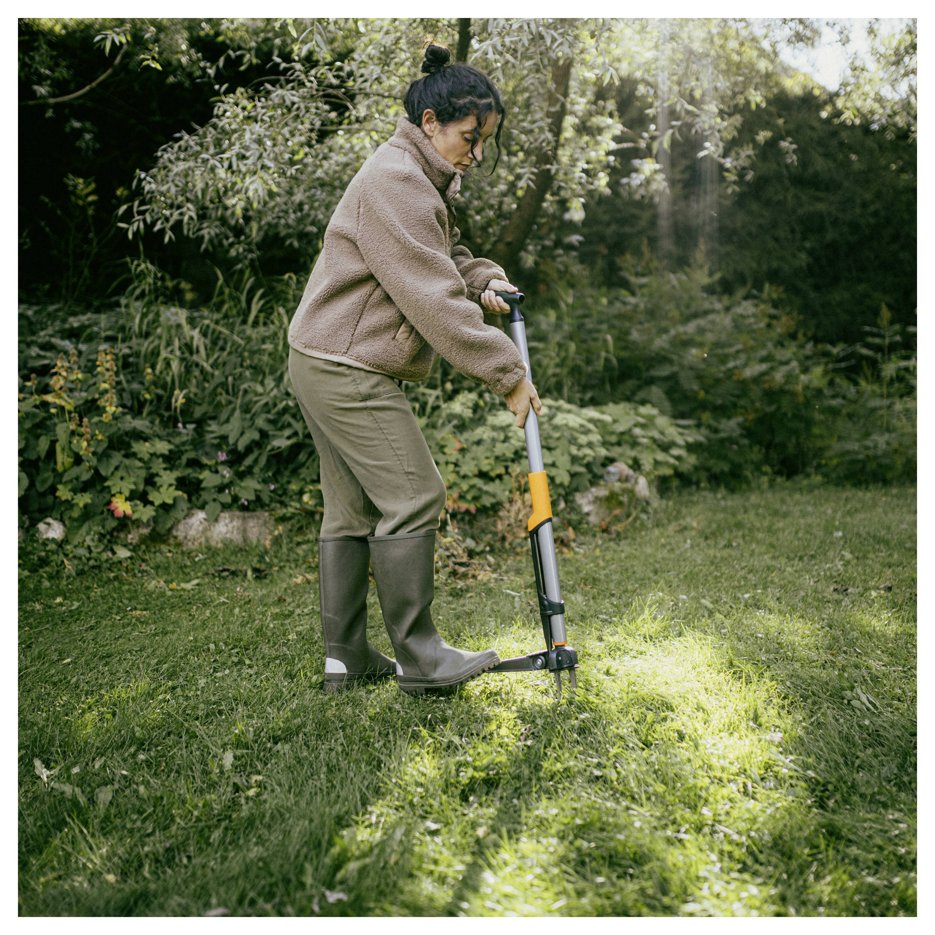 Vrouw die een handmatige grasmaaier gebruikt om een zonnig gazon in een tuin te maaien.