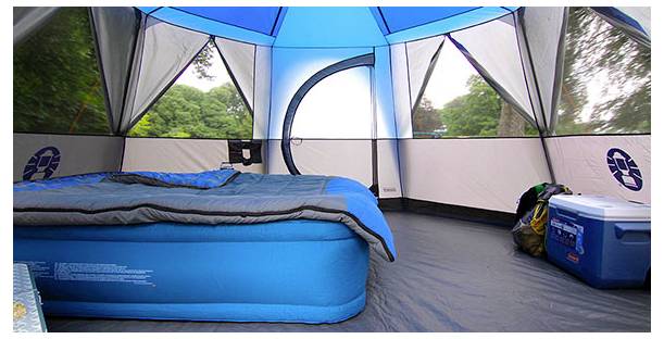 Interieur van een campingtent met een luchtmatras, slaapzak, koelbox en rugzak, gezien door de gaasvensters van de tent.