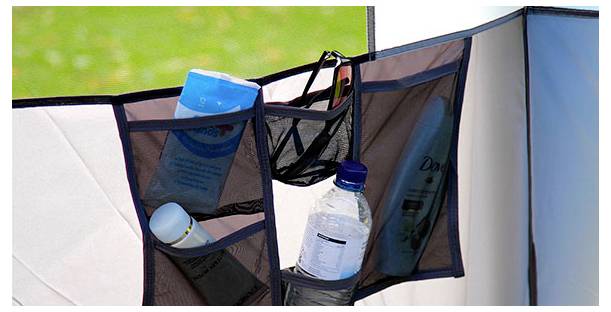 Mesh opslagorganizer die aan een tentwand hangt, met daarin een waterfles, zaklamp en ander klein kampeermateriaal.