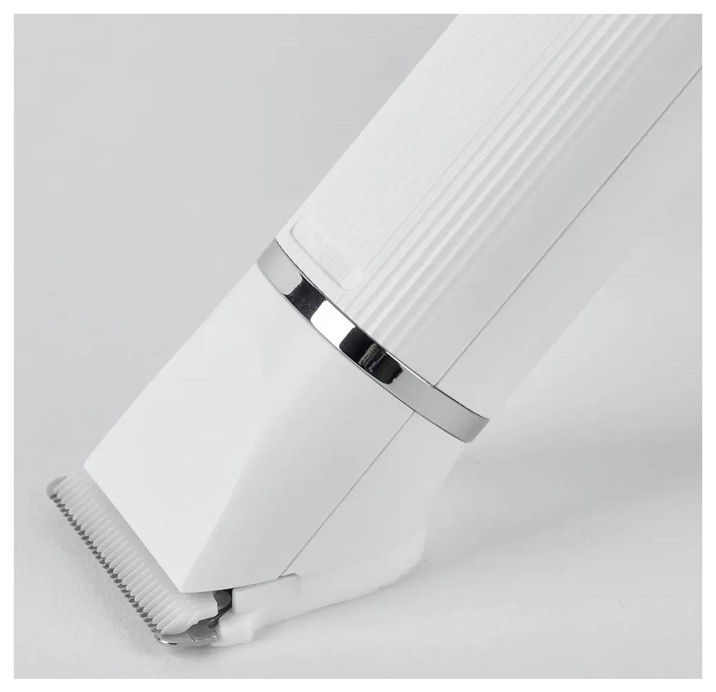 Close-up van een witte elektrische haartrimmer onder een hoek op een effen grijze achtergrond, met zicht op het metalen blad en de gestructureerde grip.