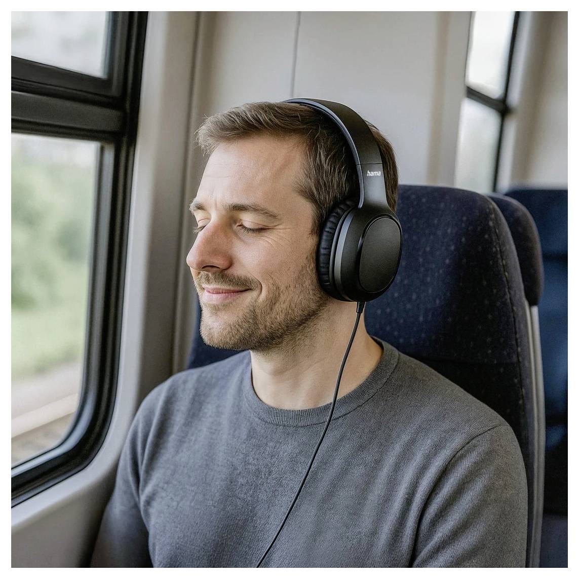 Man met over-ear koptelefoon zit bij een treinraam met gesloten ogen, ziet er ontspannen uit en luistert naar audio.