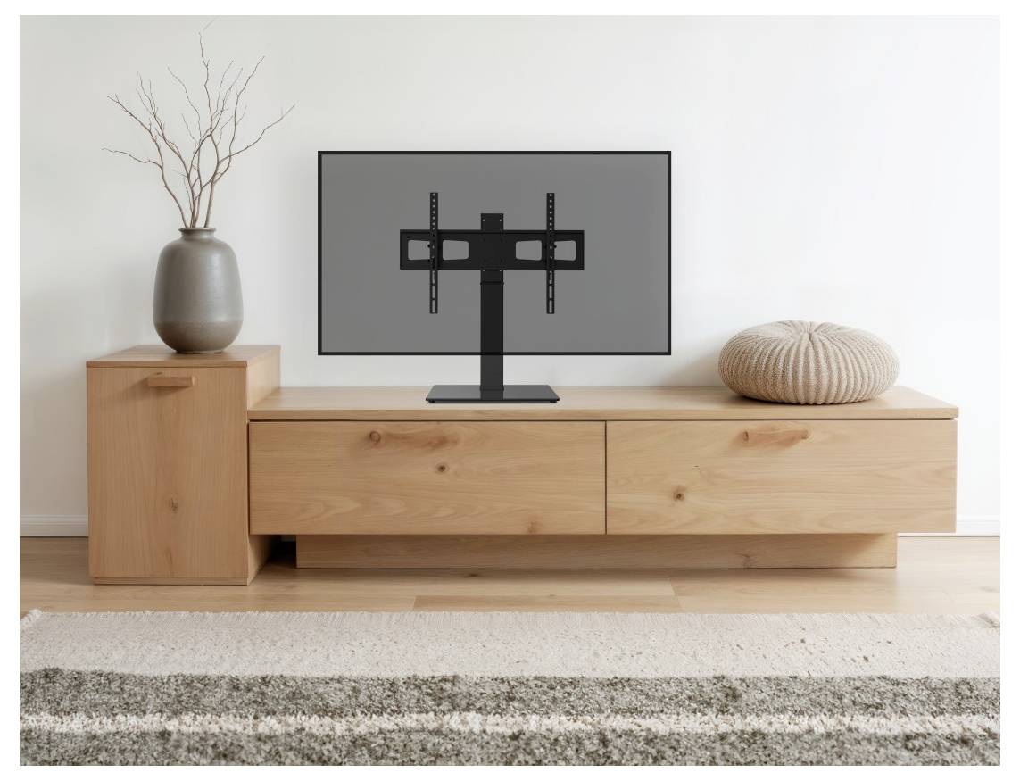 Flat-screen televisie op een laag houten mediameubel, met een vaas met takken aan de linkerkant en een rond kussen aan de rechterkant in een minimalistische woonkamer.