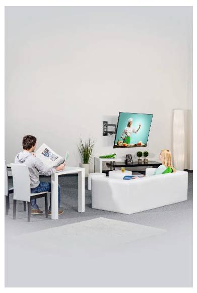 Een man leest een tijdschrift aan een tafel terwijl een kind op een bank zit en televisie kijkt in een heldere woonkamer.