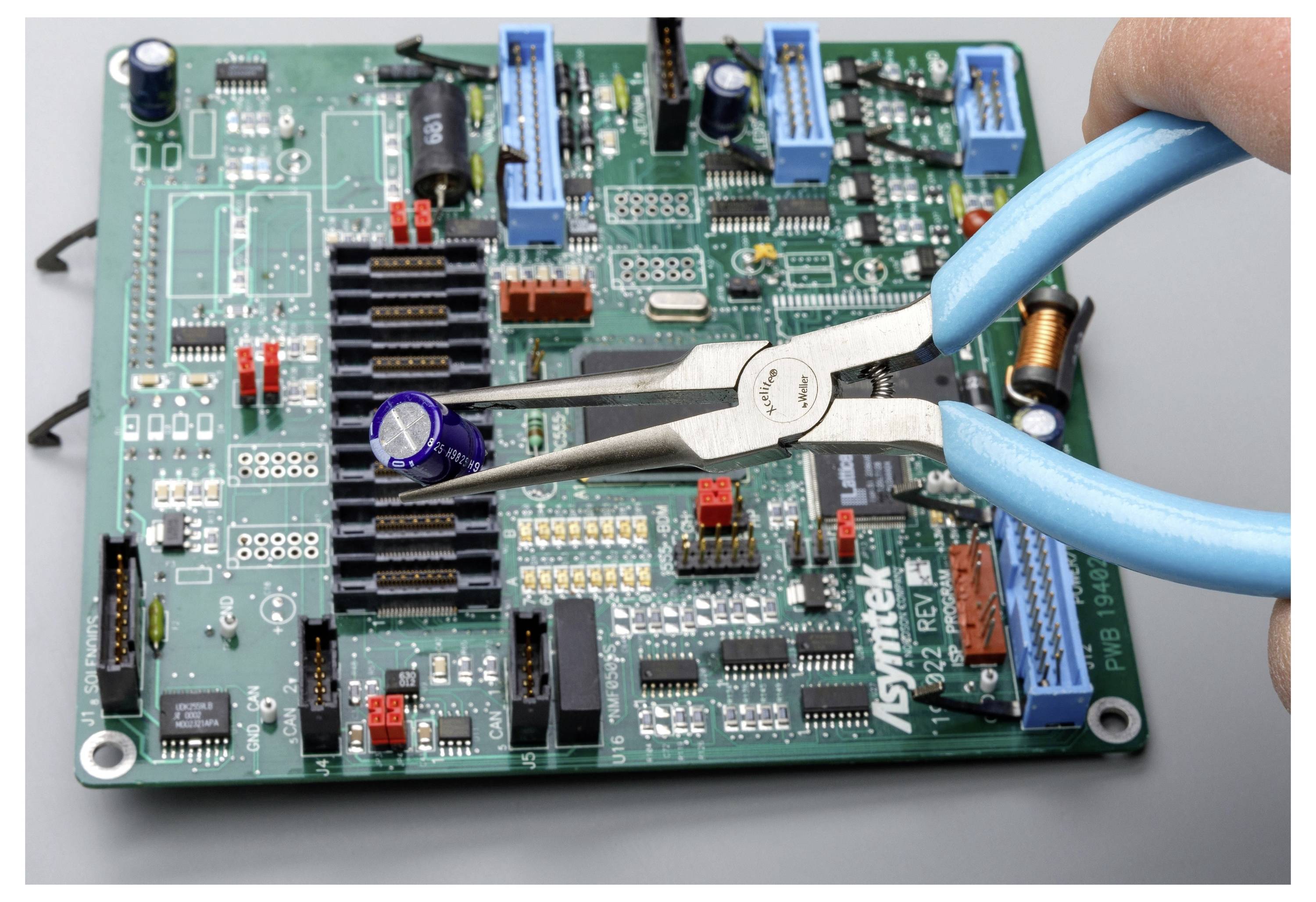 Close-up van blauwe tang die een groen printplaatje met elektronische componenten en connectoren vastgrijpt.