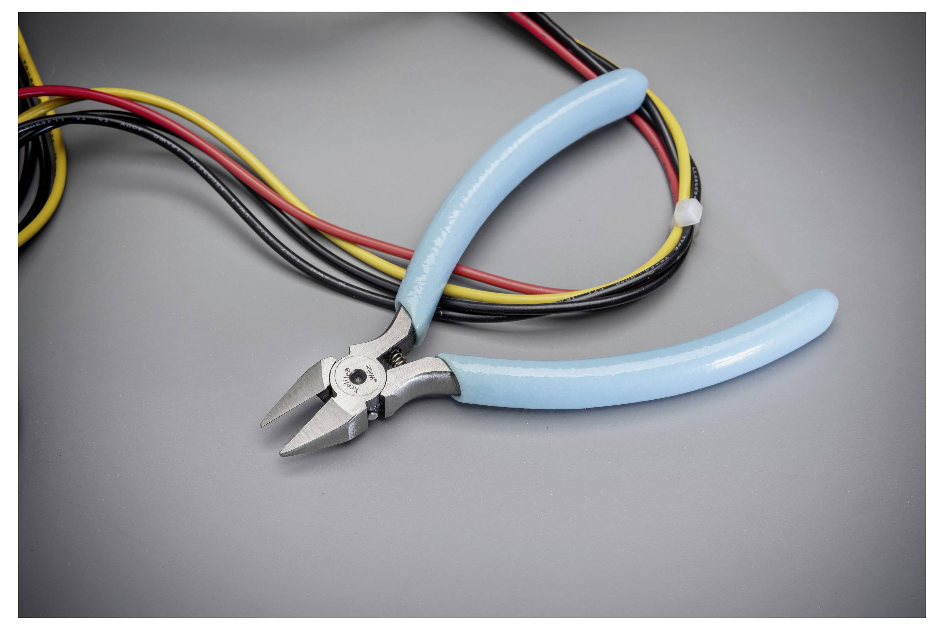 Blauwe-handvat diagonale kniptangen rustend op opgerolde veelkleurige elektrische draden op een grijs oppervlak.