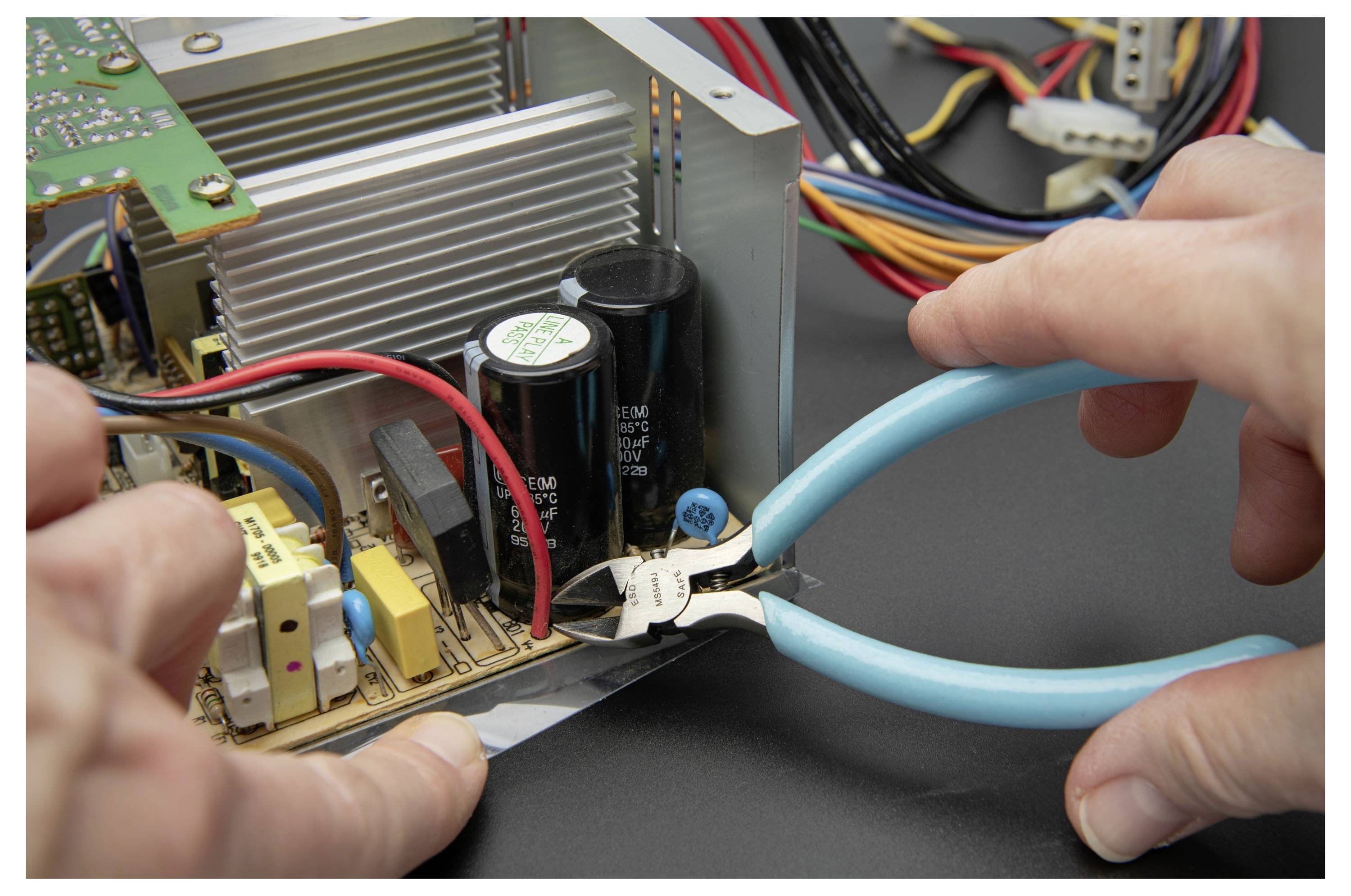 Handen die blauwe-handvat tang gebruiken om een witte kabel in een elektronisch apparaat door te knippen met blootgestelde printplaten en componenten.