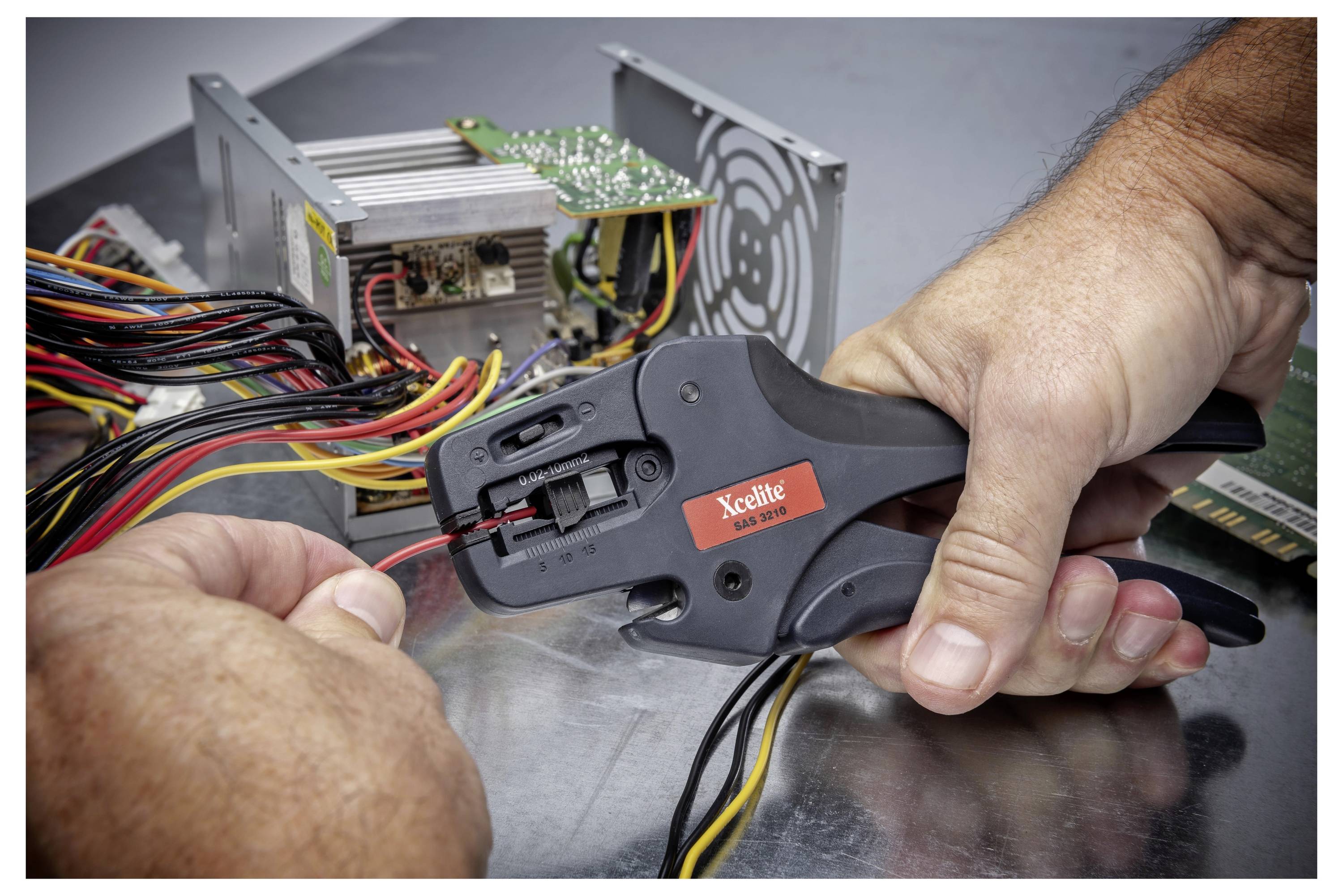Persoon die een gele draad crimpt met een Xcelite ratelende tool naast een open computervoeding en gebundelde kabels.