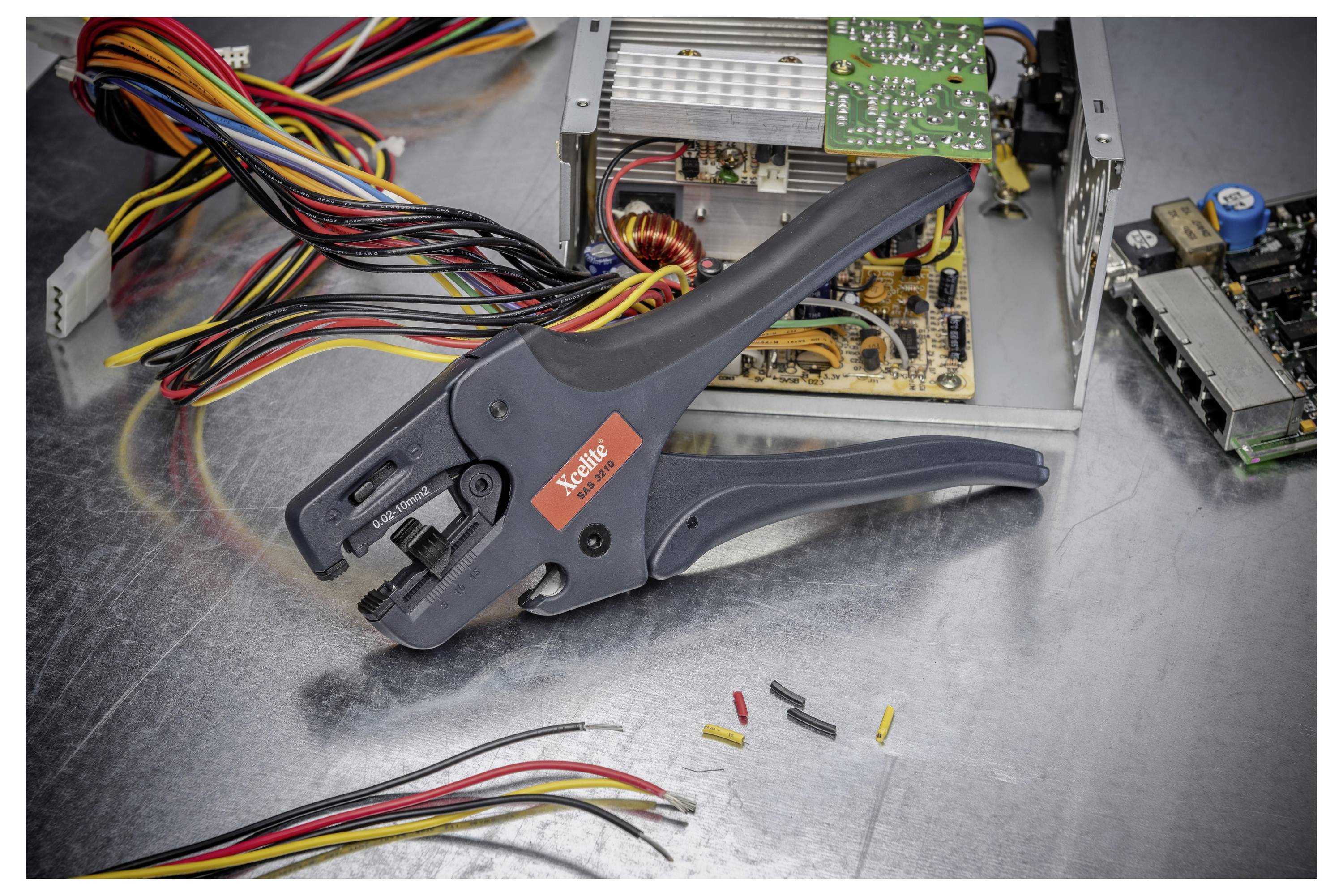 Draadkrimptang op een metalen werkbank met gekleurde kabels, losse connectors en een open elektronisch apparaat dat wordt gerepareerd.
