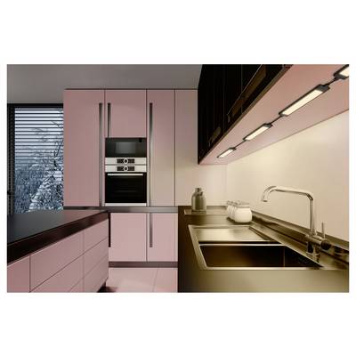 Moderne roze keuken met ingebouwde oven en kasten, gootsteen, werkblad, verlichting onder de kasten en raamgordijnen.