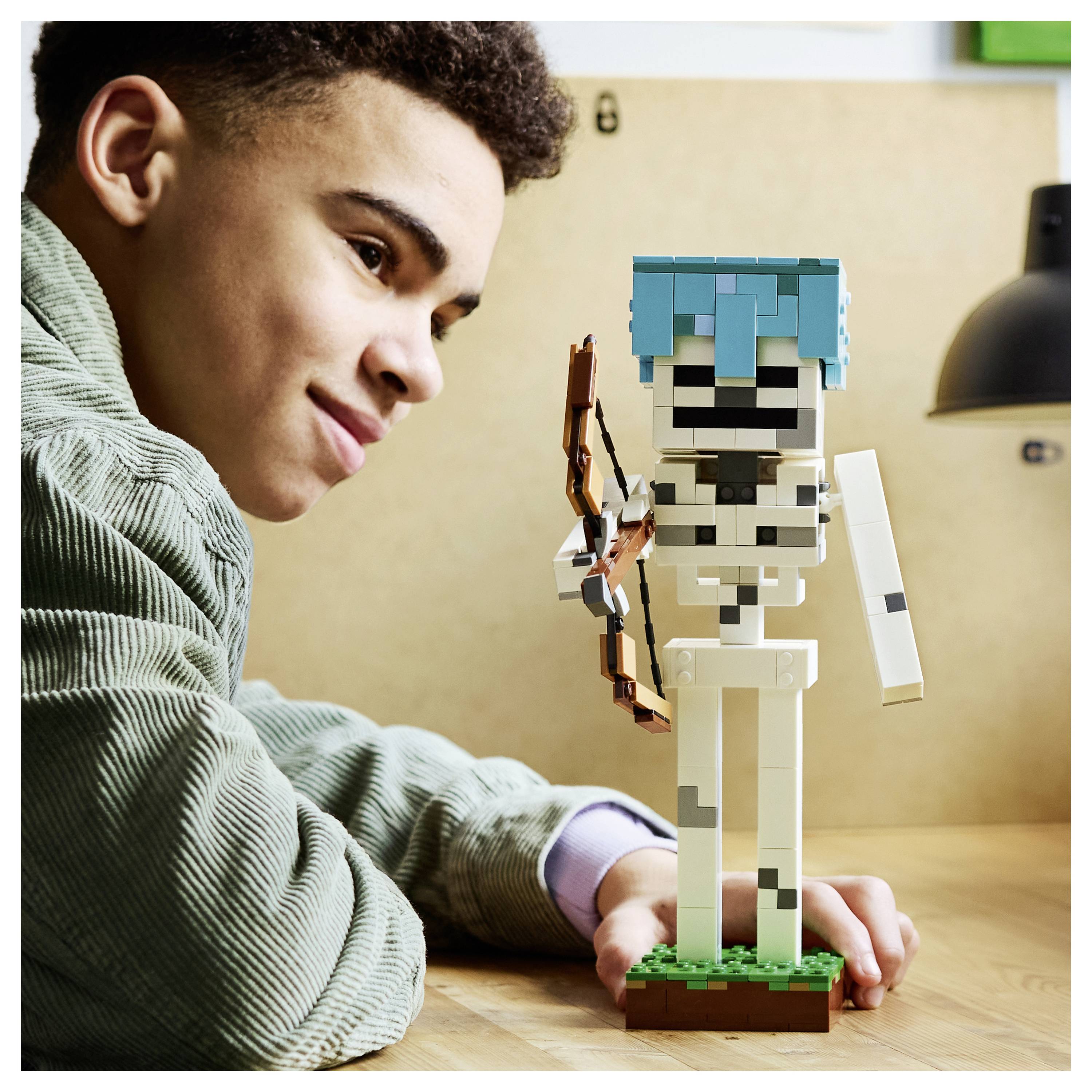 Kind kijkt naar een LEGO-achtig skeletfiguur dat hij op tafel heeft gebouwd, waarbij het model een boog vasthoudt.