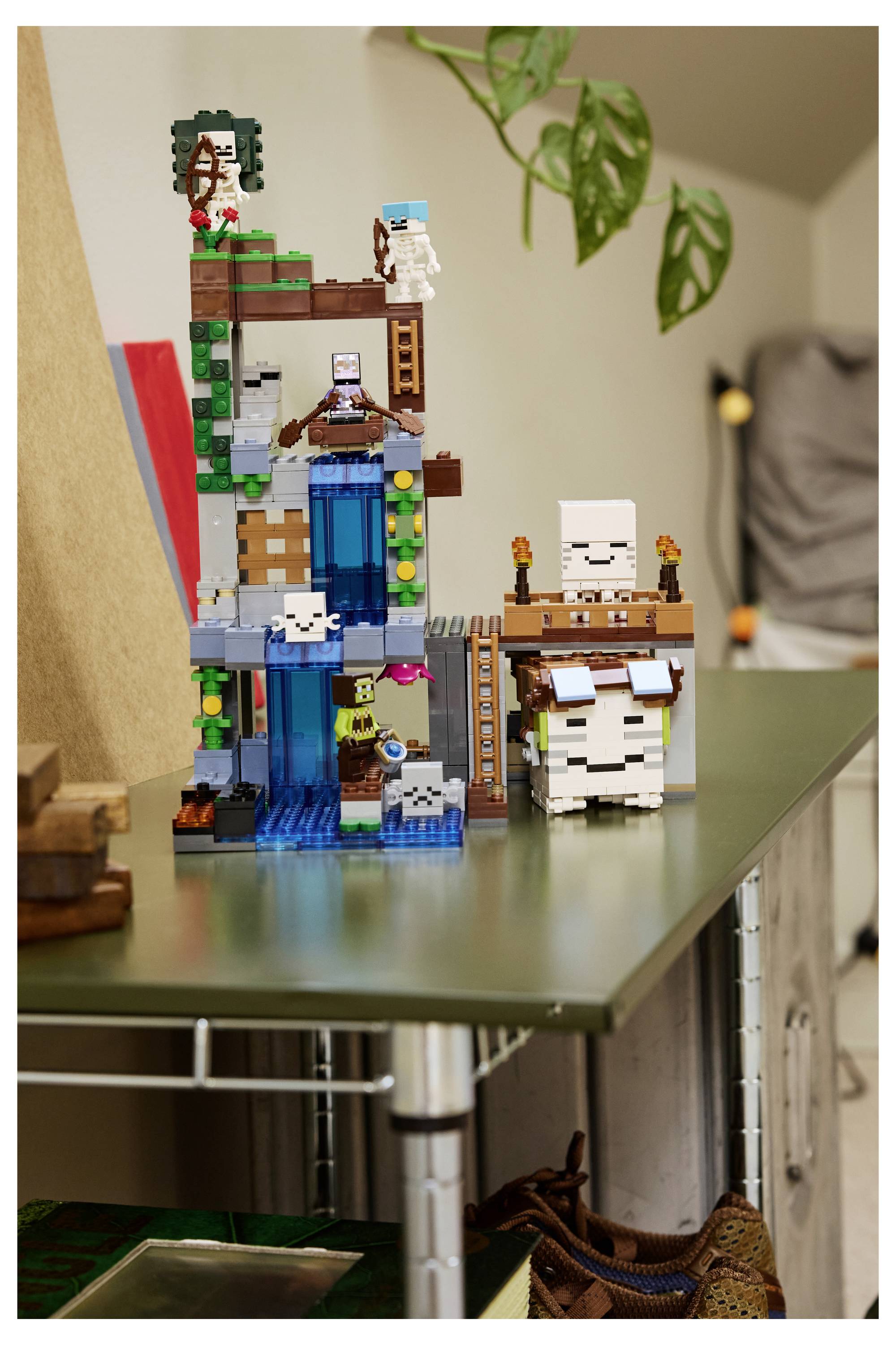 Een LEGO Minecraft-stijl fortuin met watervallen, ladders en kleine blokfiguren staat op een tafel binnenshuis.