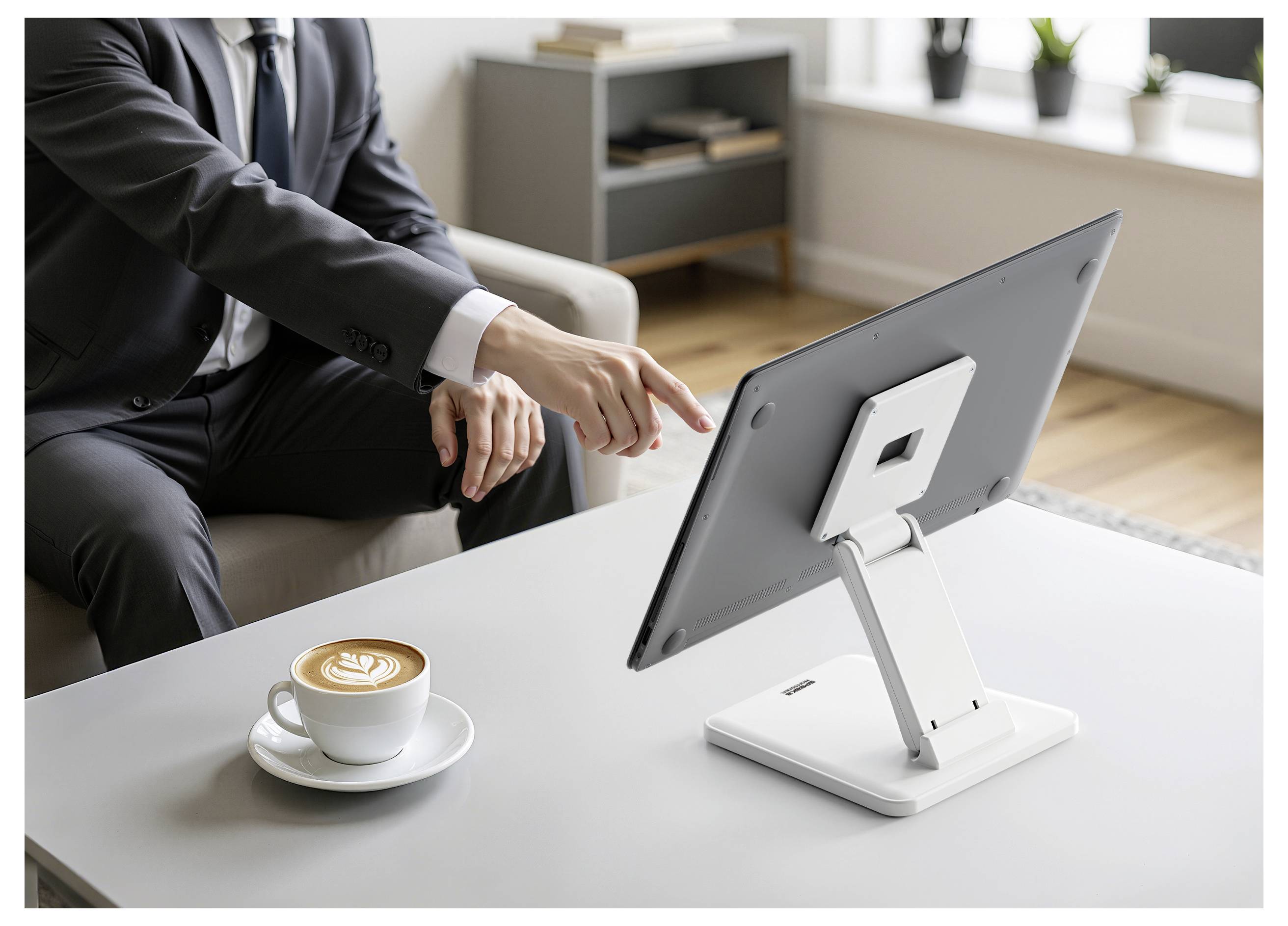 Zakenman in een pak wijst naar een desktopmonitor op een witte tafel naast een kopje koffie in een kantooromgeving.
