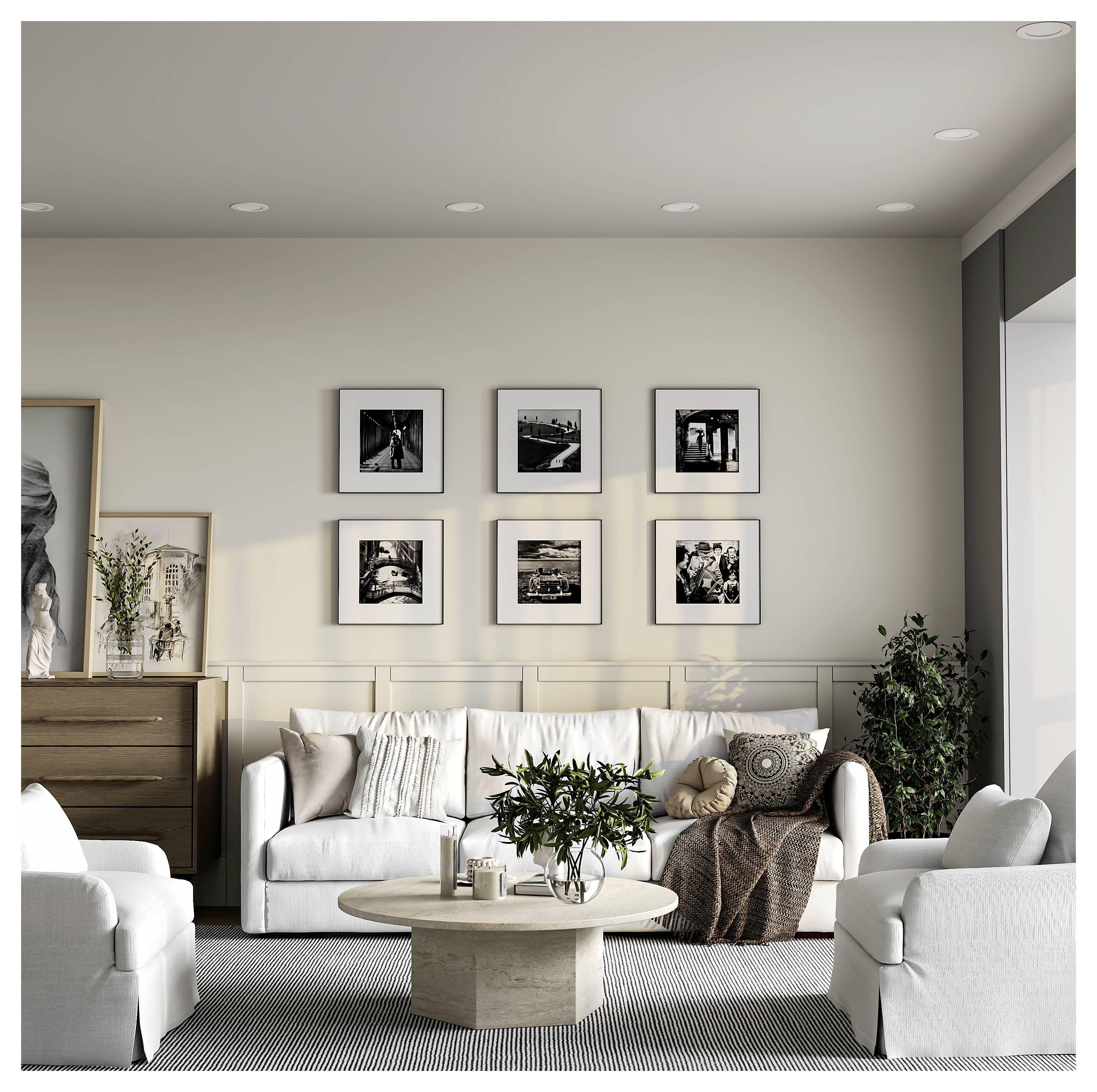 Moderne woonkamer met witte banken, ronde salontafel, dressoir, potplanten en zes ingelijste zwart-witfoto's aan de muur.