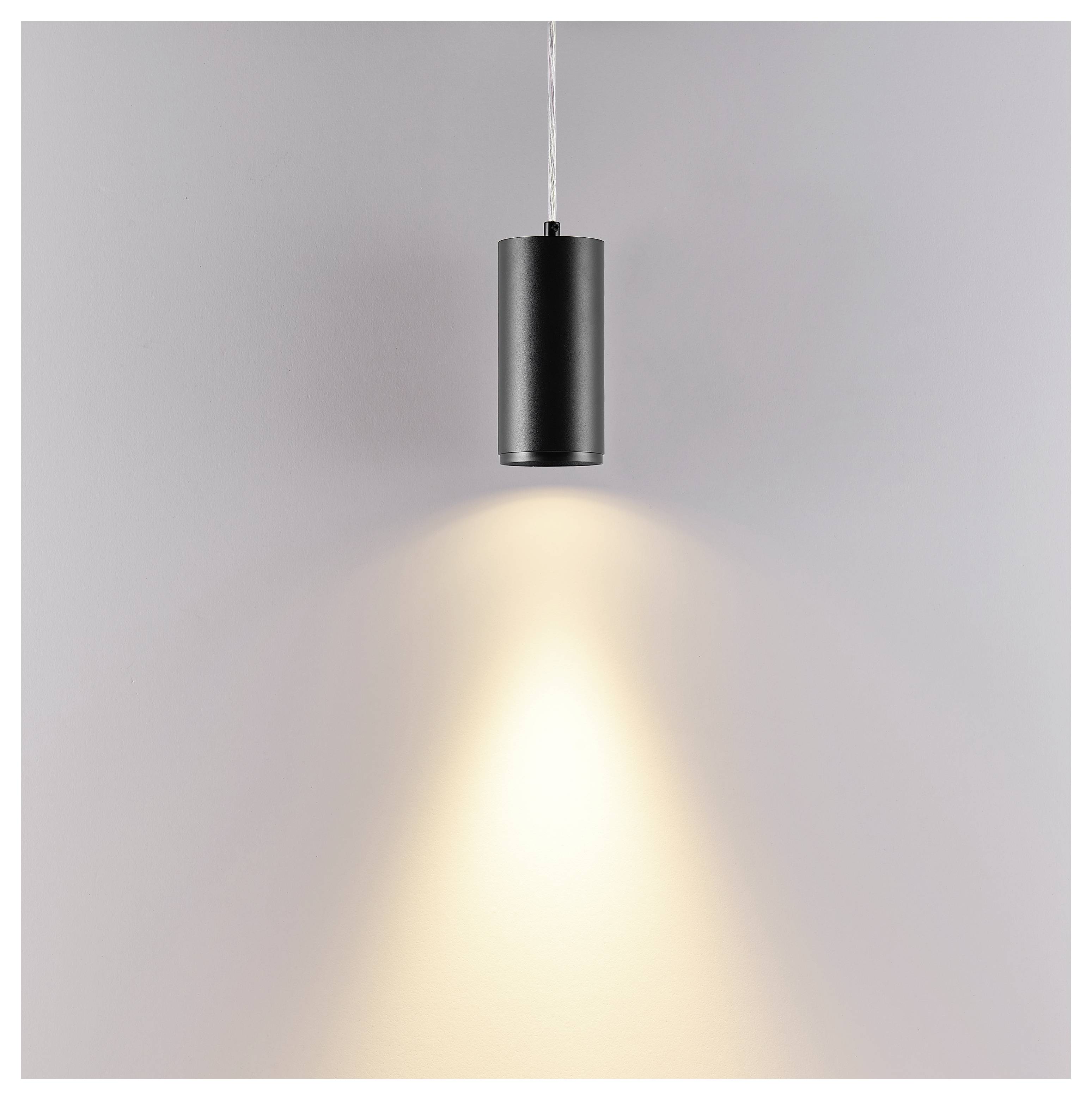 Zwarte cilindrische hangende lamp die een warme lichtkegel op een eenvoudige muur werpt.