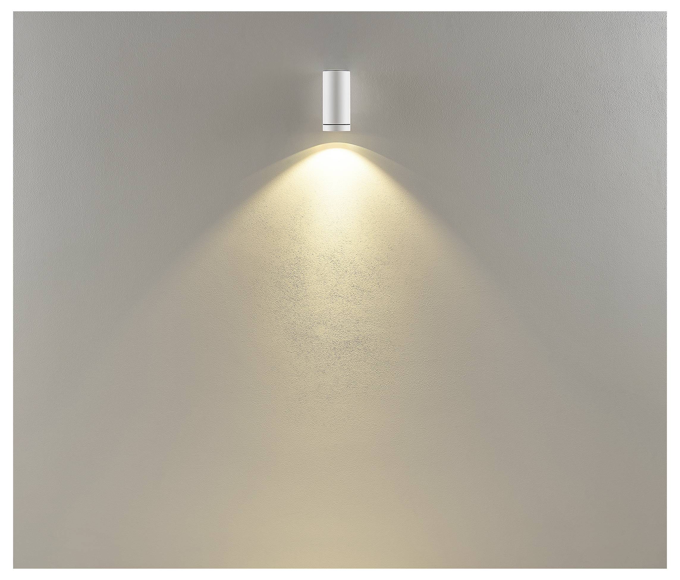 Aan de muur gemonteerde zilveren verlichtingsarmatuur dat een warme lichtkegel op een effen beige muur werpt.