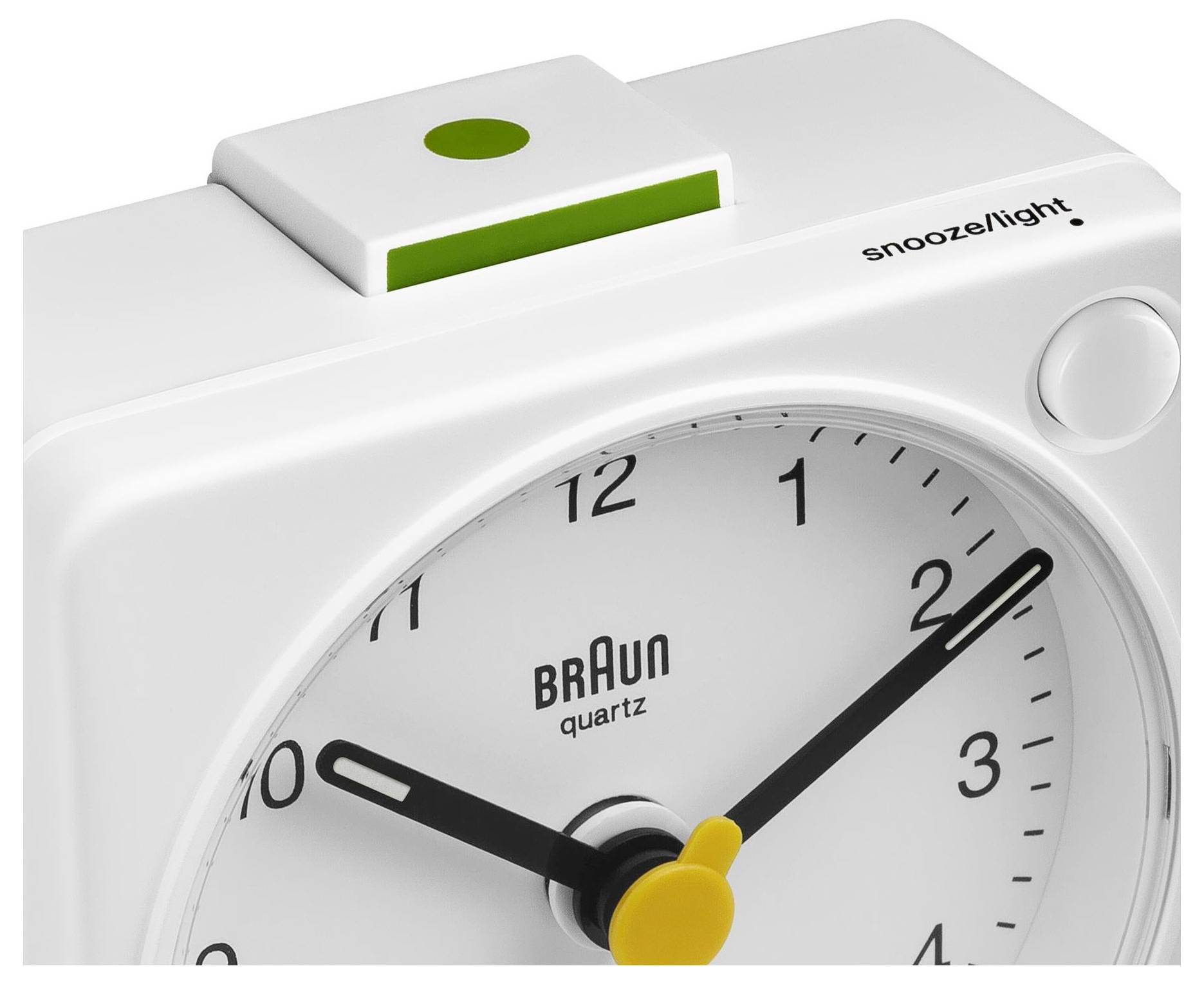 Close-up van een wit Braun kwarts wekker met 'snooze/light'-knop en gele wijzers, die ongeveer 2:50 aangeeft.