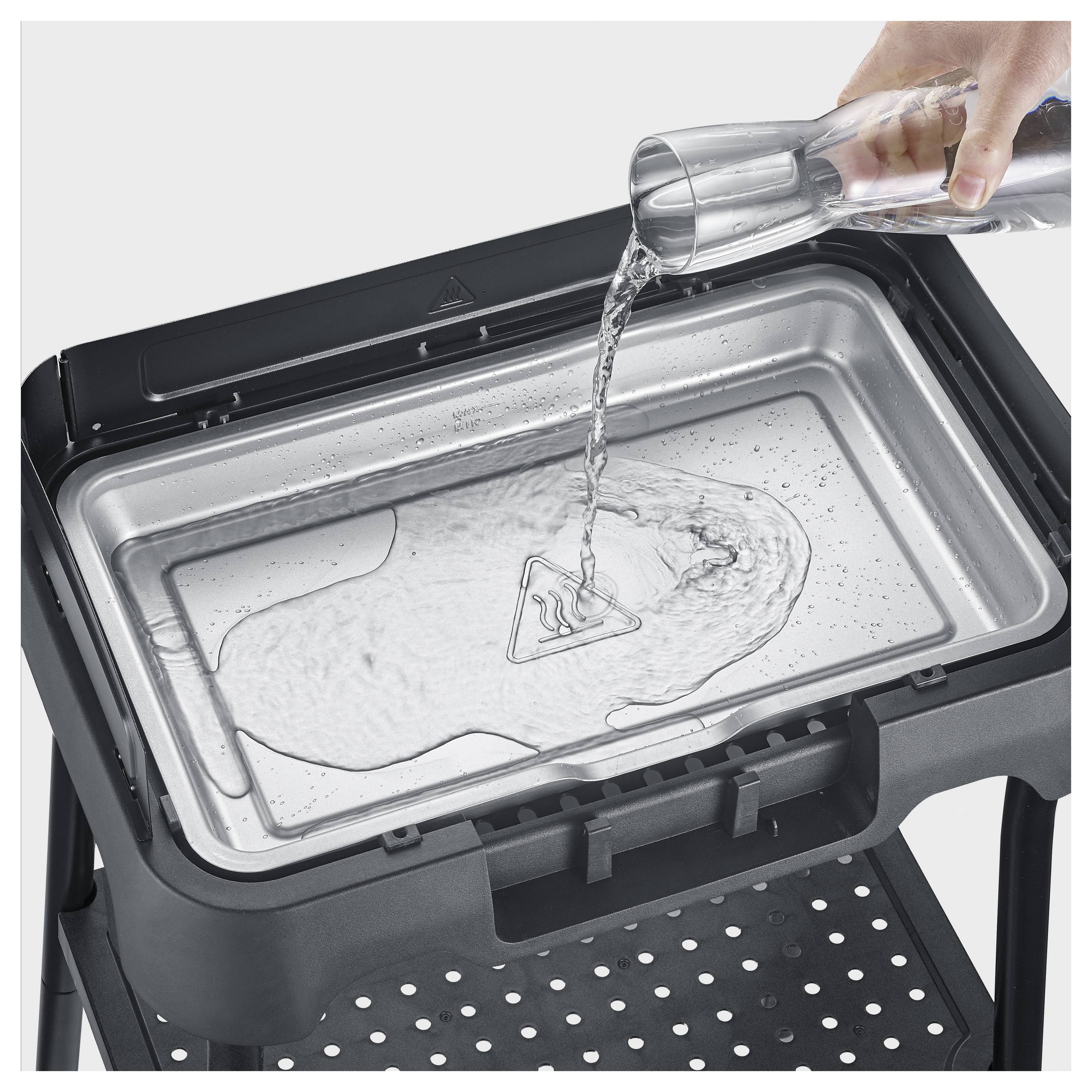 Een hand giet water uit een glas in een verwijderbaar apparaatbakje, wat een vullings- of reinigingsactie toont.