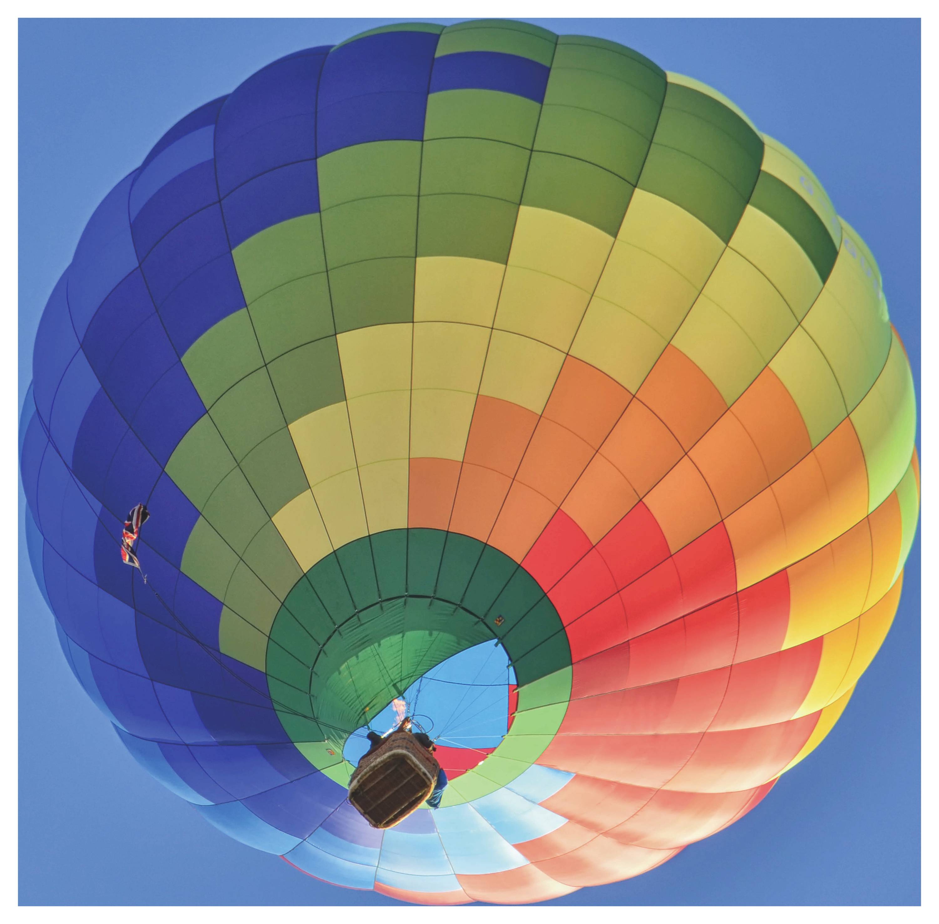 Kleurrijke heteluchtballon van onderaf gezien tegen een heldere blauwe lucht, met een regenbooggestreepte ballon en mand.