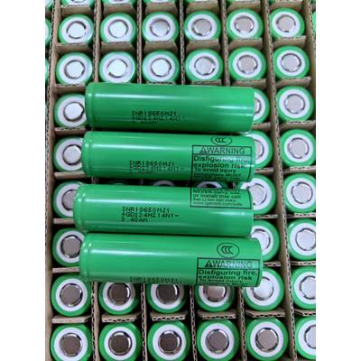 Gestapelde groene lithium-ion batterijen in kartonnen bakken, met verschillende grotere cellen voorzien van waarschuwingstekst over brand- en explosierisico's.