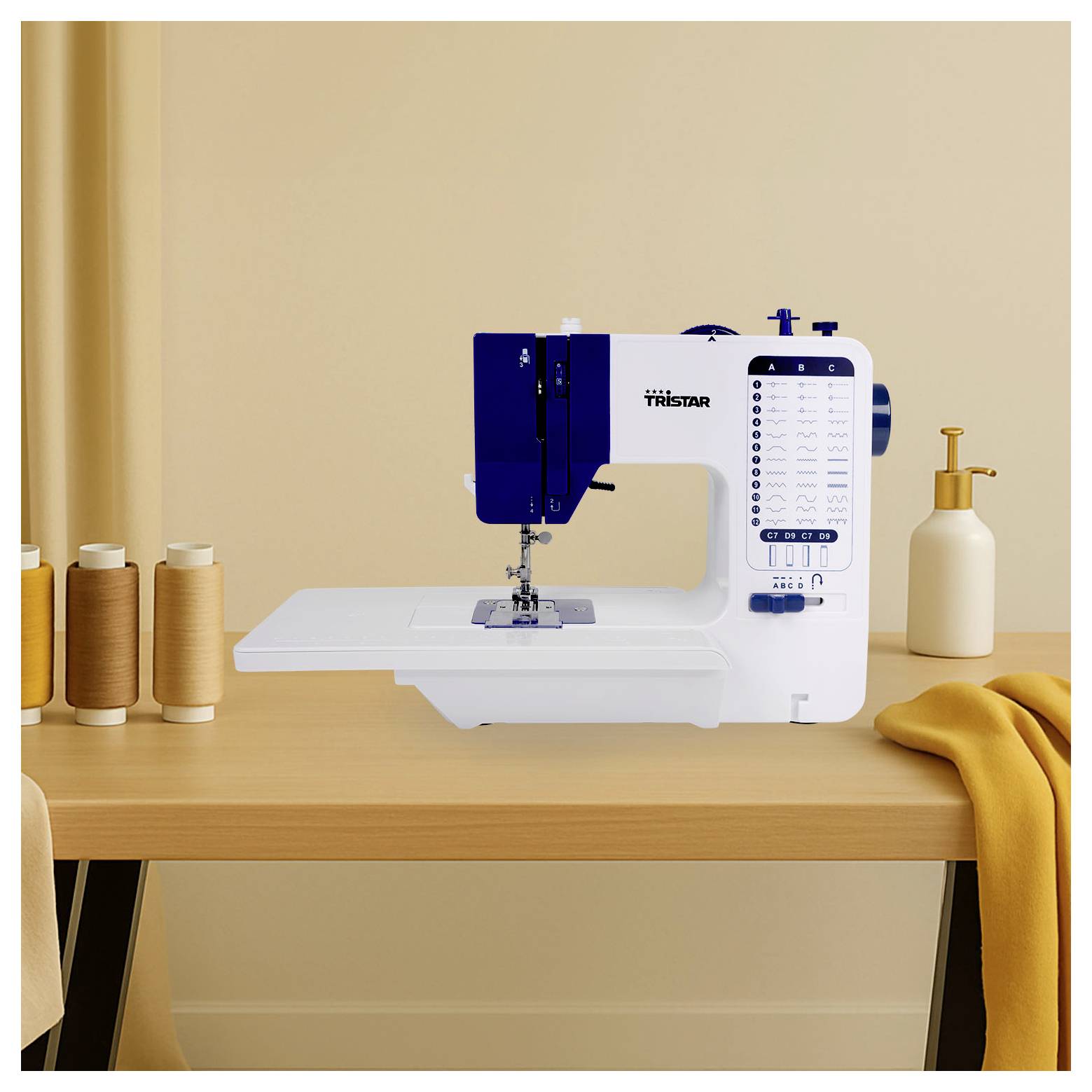 Wit-en-blauwe Tristar naaimachine op een houten tafel met spoelen garen en opgevouwen geel stof ernaast