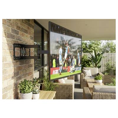 Flatscreen-tv gemonteerd op een bakstenen patiomuur, waarop een voetbalwedstrijd wordt weergegeven in een buitenzitgedeelte met rotan meubilair en planten.
