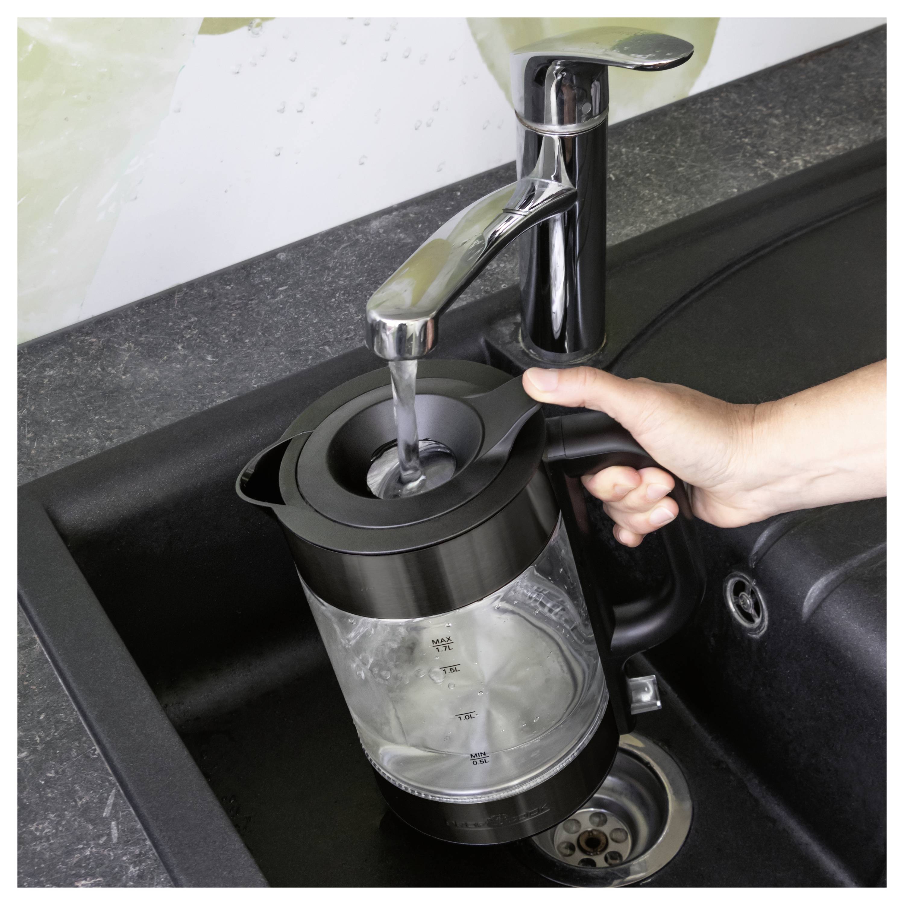 Een hand vult een zwart elektrisch waterkoker met water uit een keukenkraan in een gootsteen.