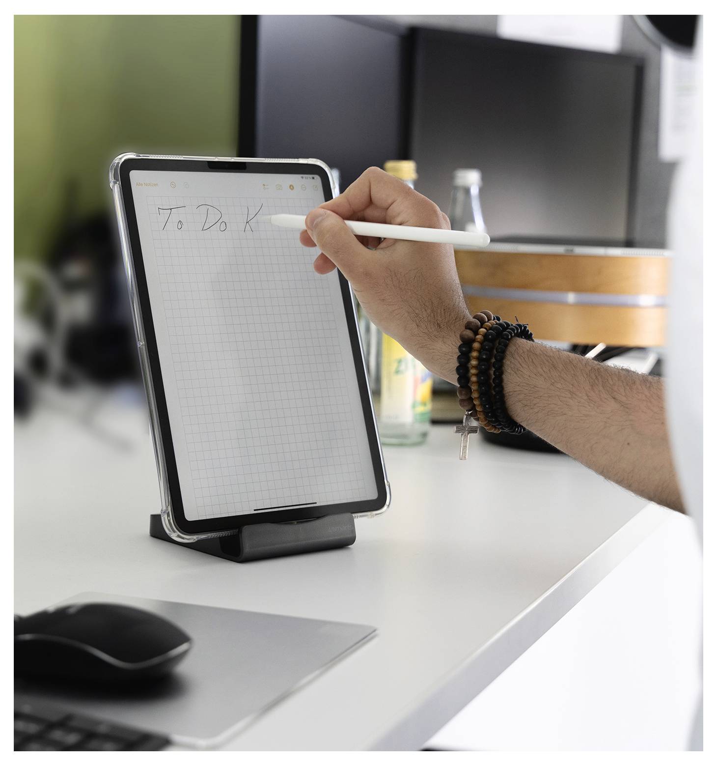 Hand schrijven 'To Do' op een tablet die op een bureau staat, met een muis en computer op de achtergrond.