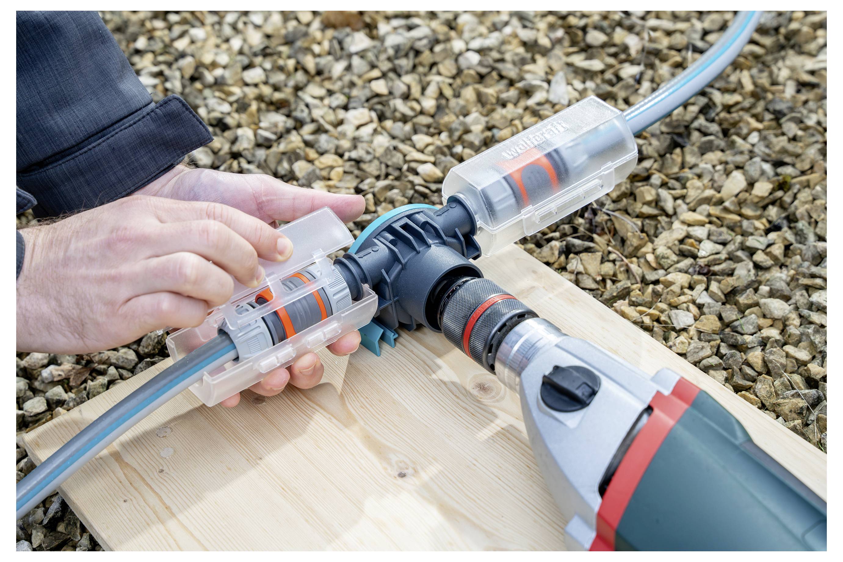 Handen die tuinslangconnectoren verbinden terwijl ze een boormachineaangedreven slangreparatiewerktuig op een houten plank buiten gebruiken.