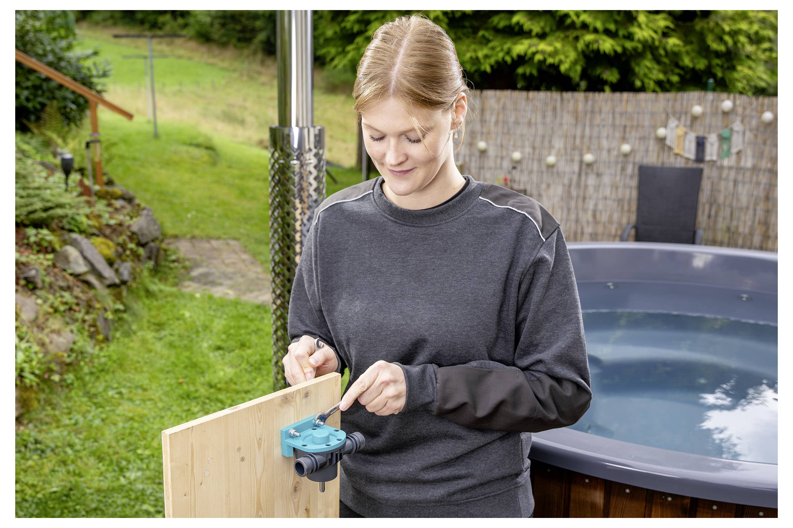Vrouw die buiten naast een hottub een houten paneel in elkaar zet, met behulp van een blauw spanklemgereedschap.