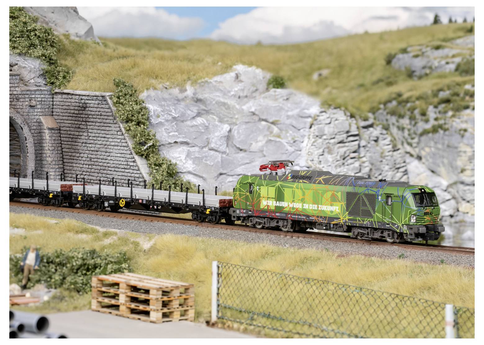 Groene locomotief die vrachtrijtuigen door een rotsachtig berglandschap trekt op een modelspoorbaan.