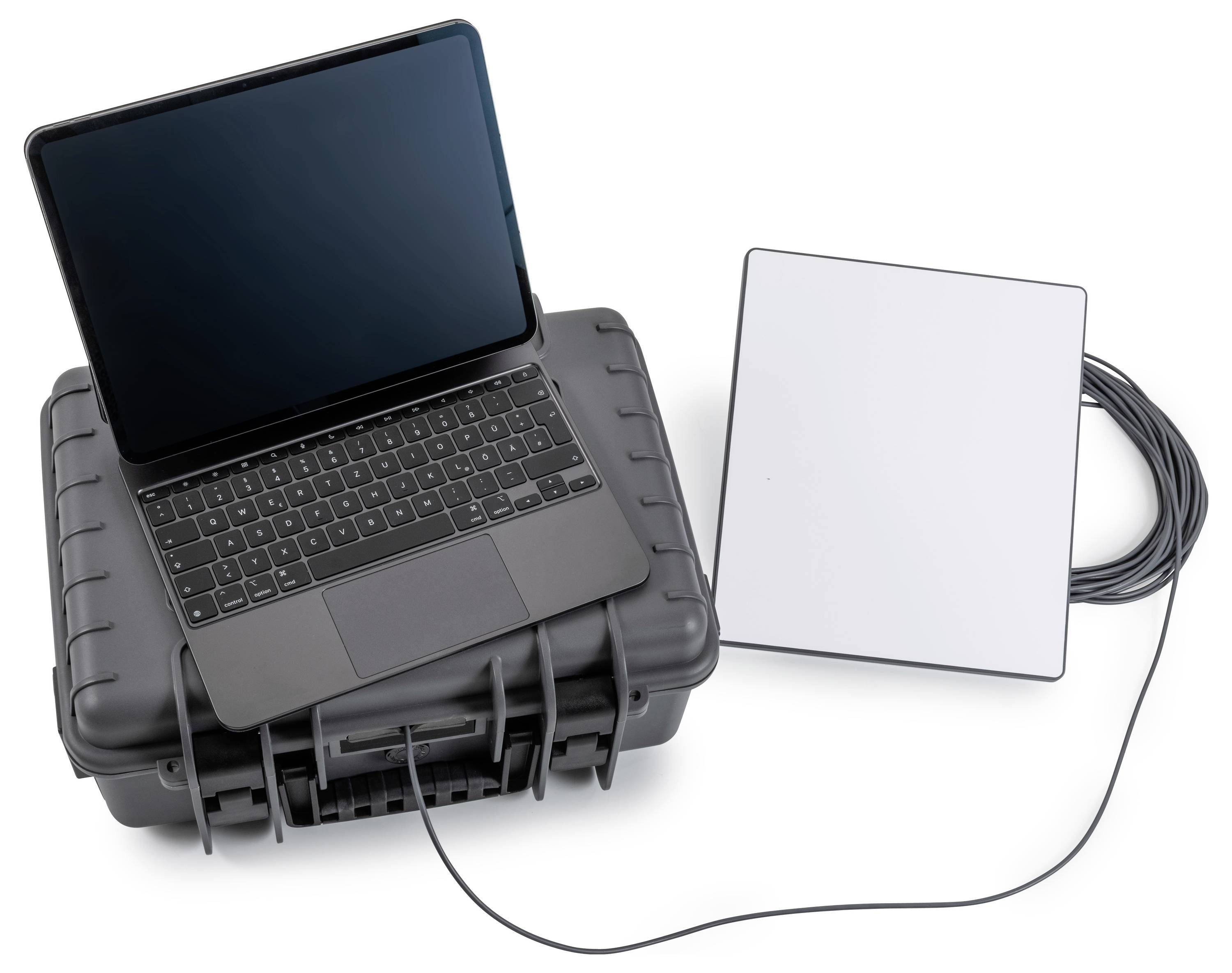 Laptop op een robuuste draagtas naast een aangesloten wit extern apparaat en kabel, wat op veld- of mobiele netwerkingsapparatuur duidt.