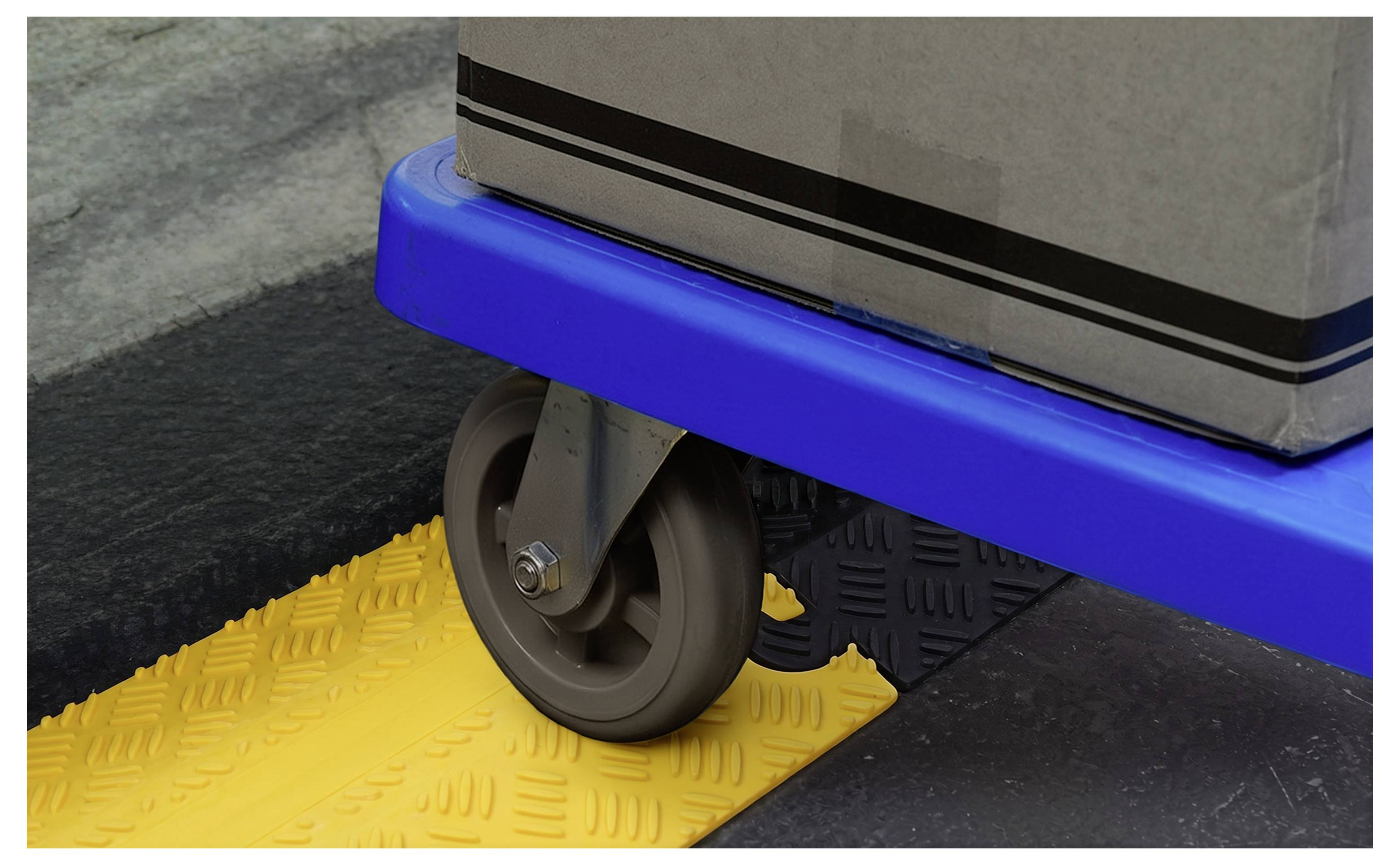 Close-up van een karwieltje dat over een gele gestructureerde helling rolt op een blauw platform, met een grijze lading die hierboven is bevestigd.