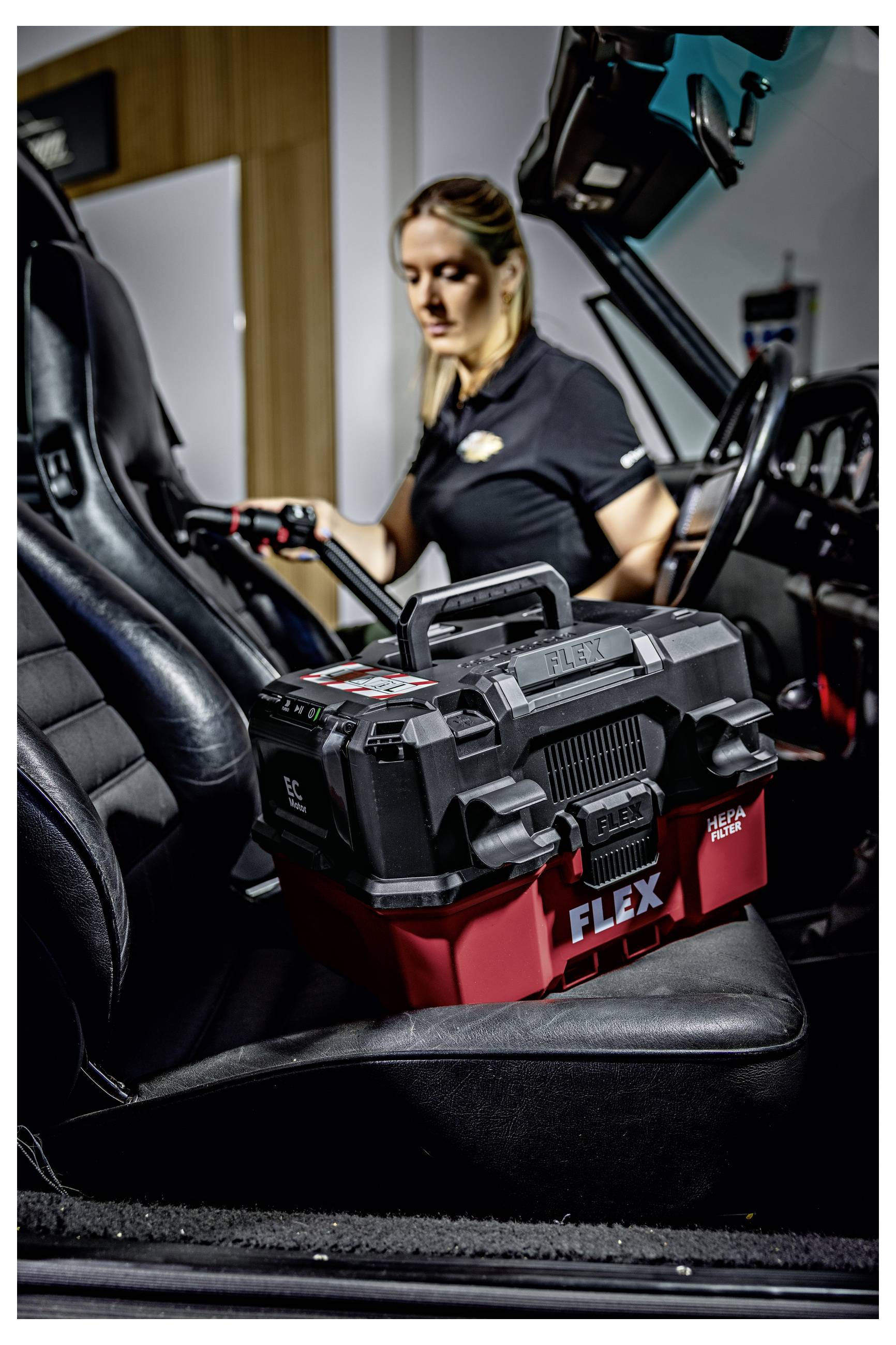 Een vrouw laadt een FLEX-gereedschapskoffertje in een auto, met de open deur en zwart lederen interieur zichtbaar.