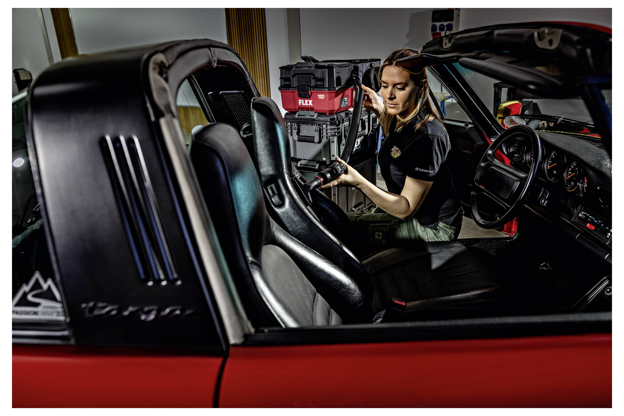 Monteur die in een rode sportwagen werkt, elektrische gereedschappen gebruikt terwijl de deuren open zijn in een autowerkplaats.