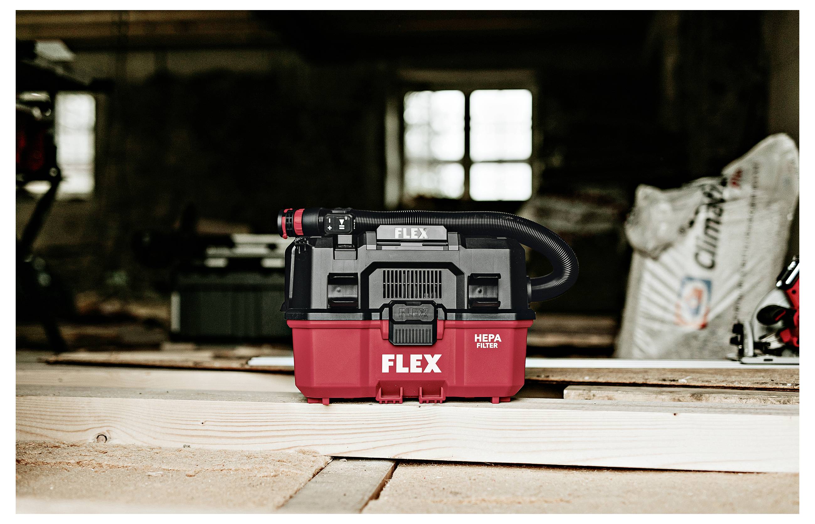 Een rood en zwarte FLEX nat/droog werkstofzuiger staat op een houten werkbank in een donkere werkplaats.