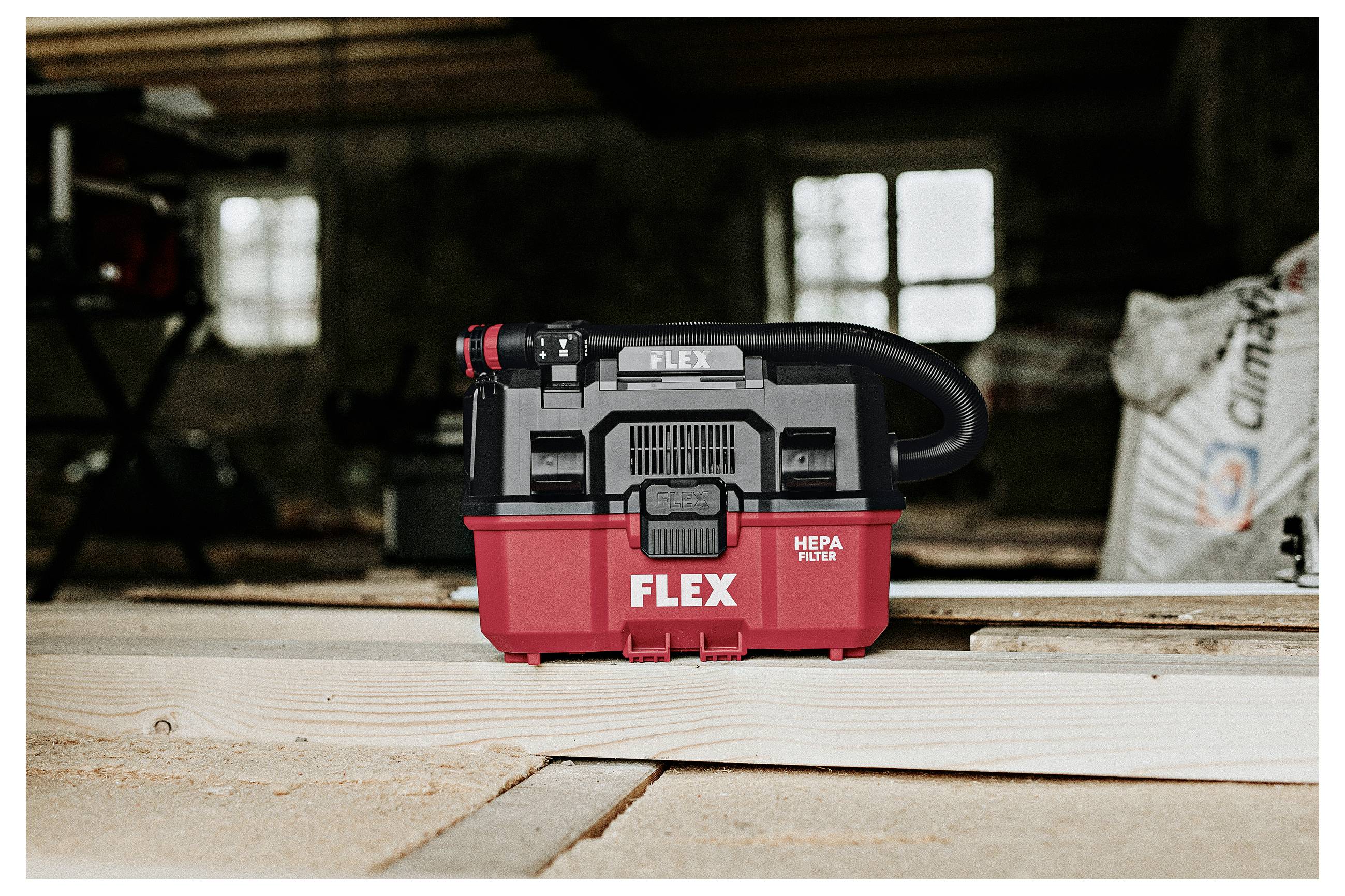 Rode en zwarte FLEX HEPA-filterstofzuiger staande op houten planken in een schemerige werkplaats of garage.