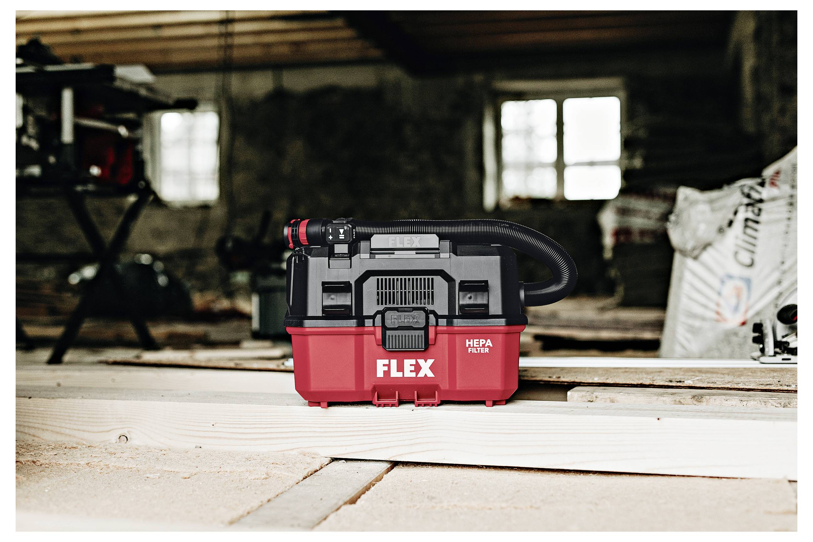 Rode FLEX HEPA-filterstofzuiger staande op houten planken in een werkplaats of bouwplaats.